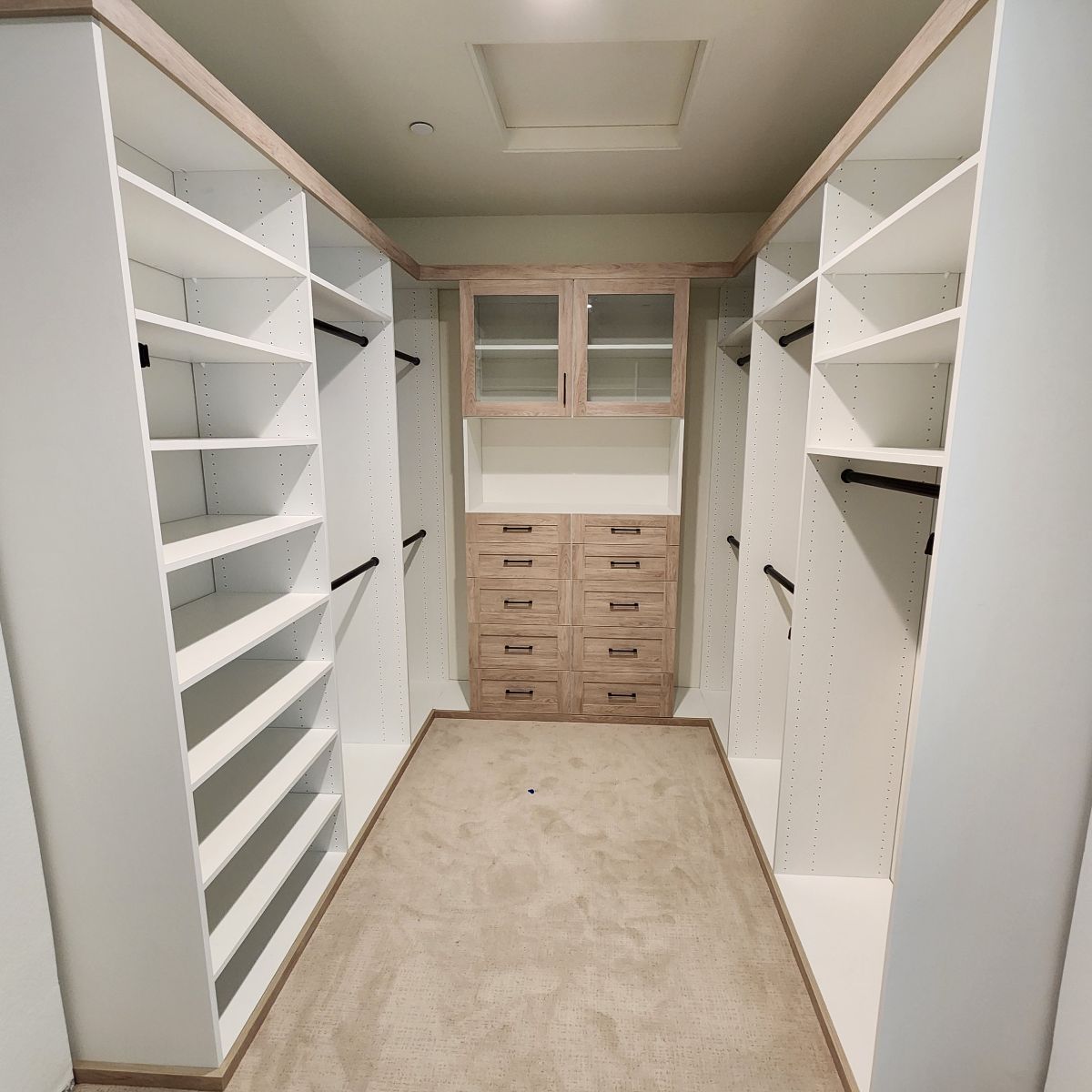 Walk-in closet with white shelves, beige drawers, and clothing rods. Center features drawers and cabinet.