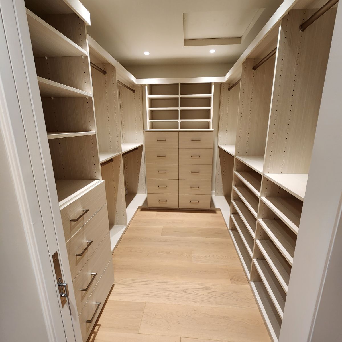 A modern, organized walk-in closet with light wood shelves and drawers.
