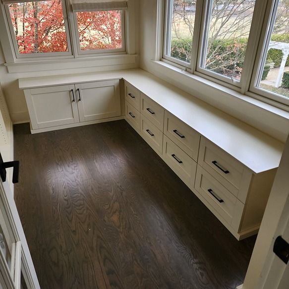 A room with white cabinets and drawers and a window