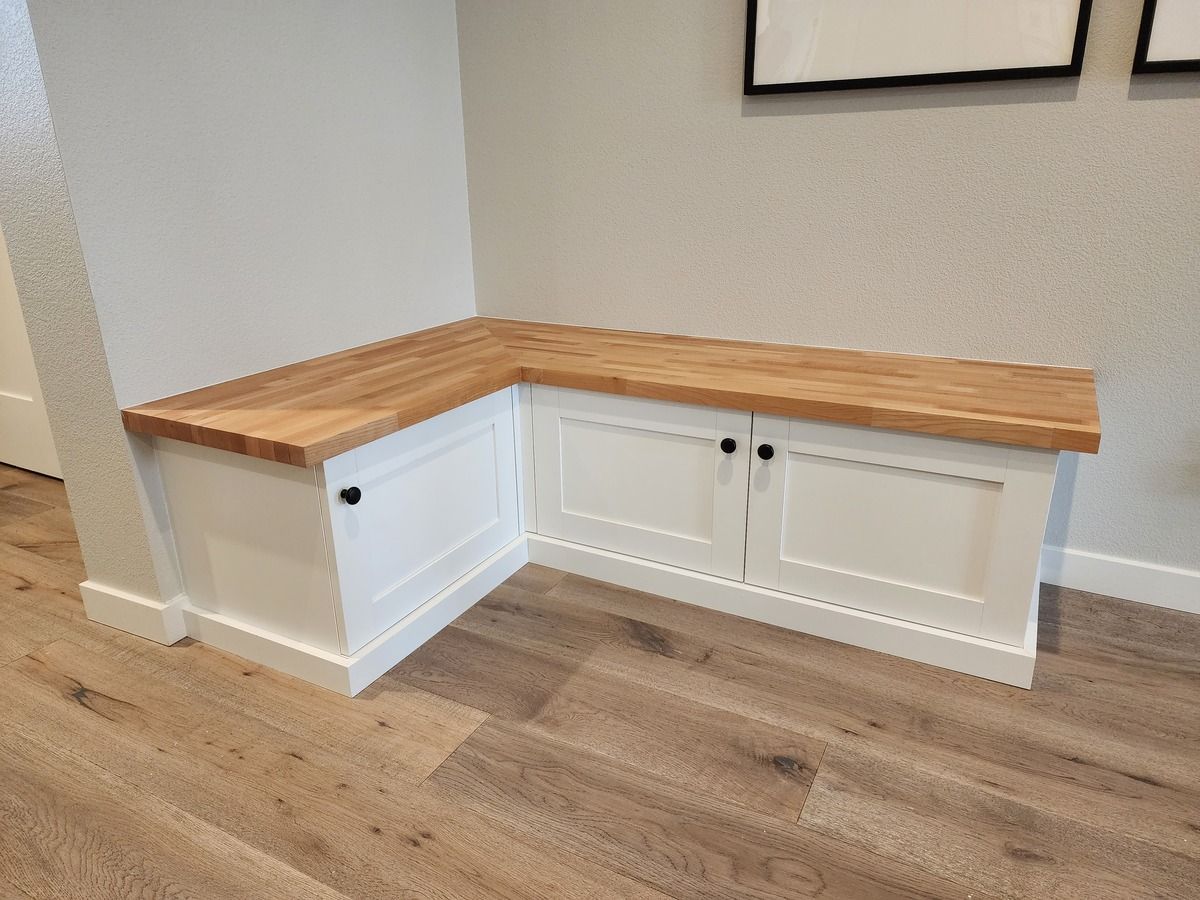 A corner bench with a wooden top and white cabinets in a hallway.