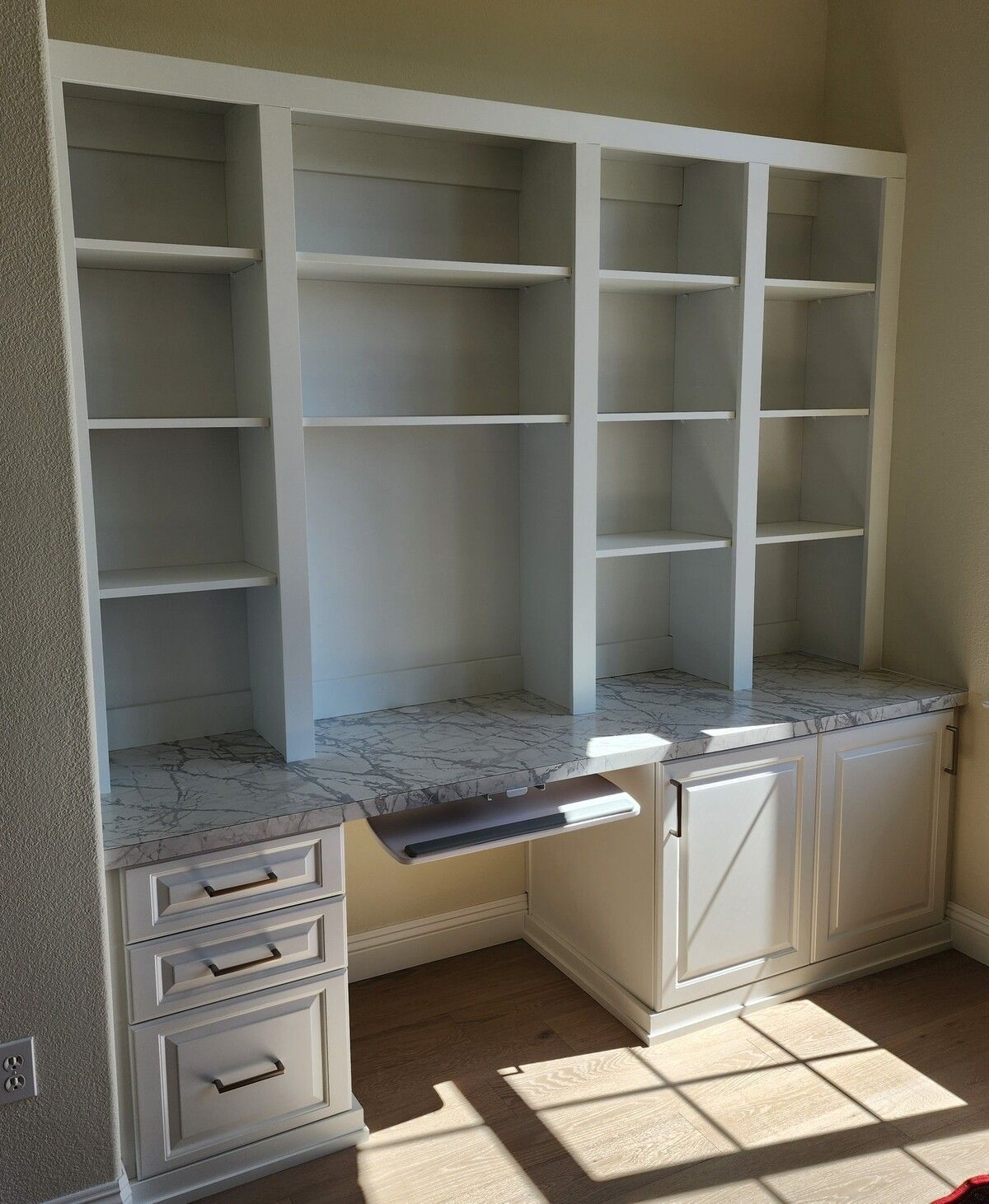 A room with a desk , shelves , drawers and a window.