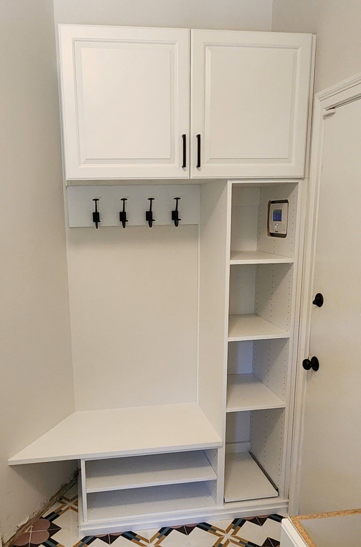 A white cabinet with hooks and shelves in a hallway.
