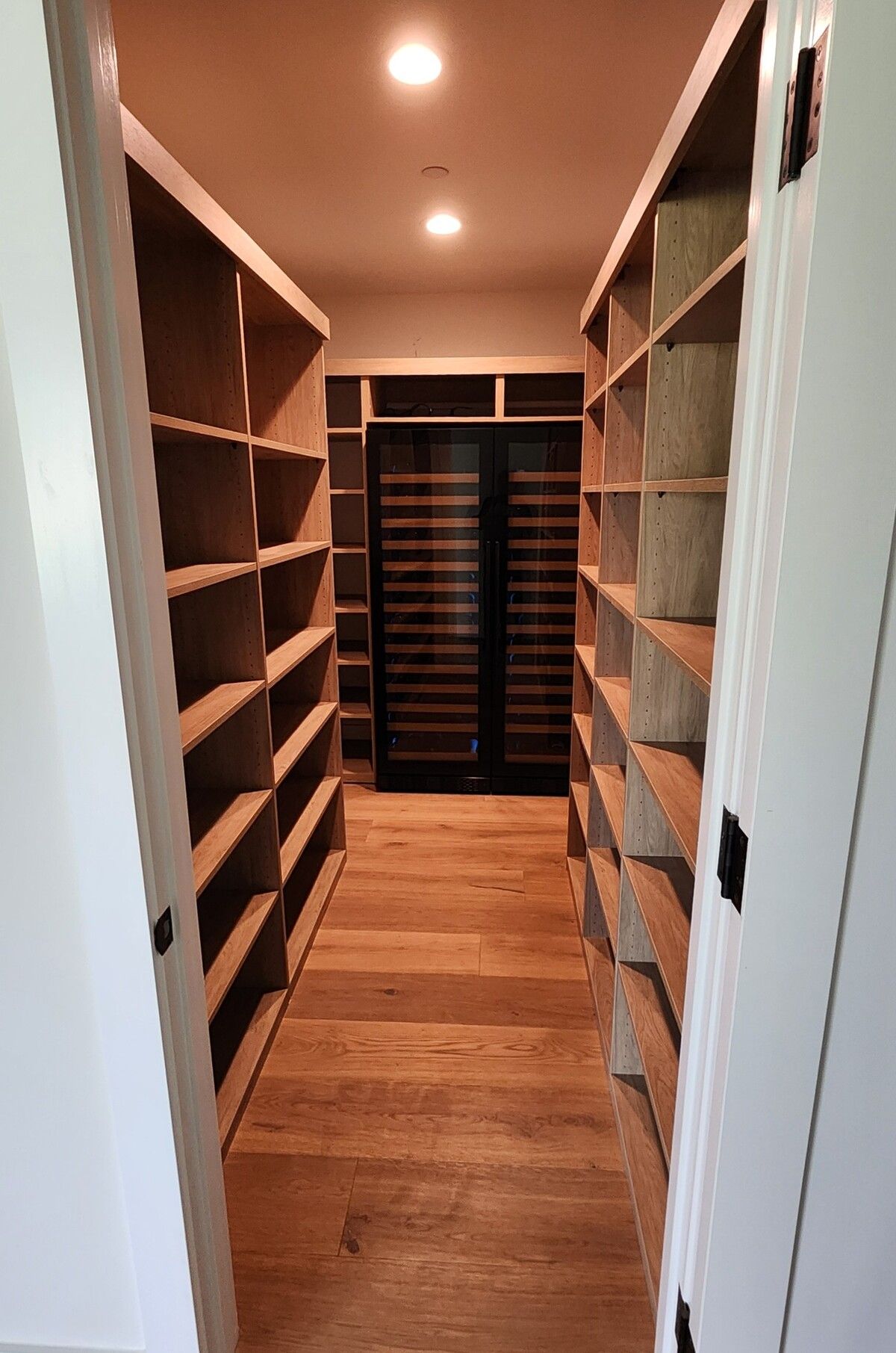 A walk in closet with wooden shelves and a wine cooler.