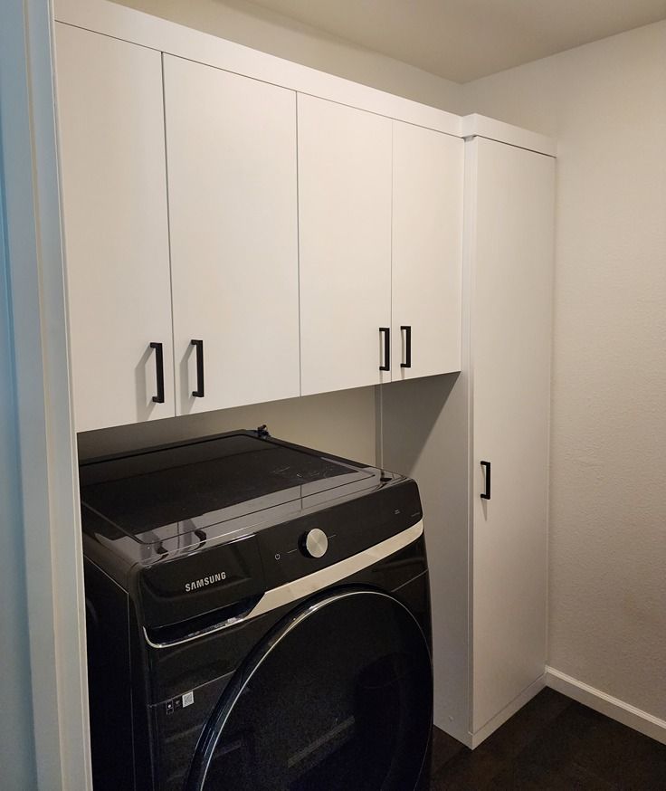 A washer and dryer are in a laundry room with white cabinets.