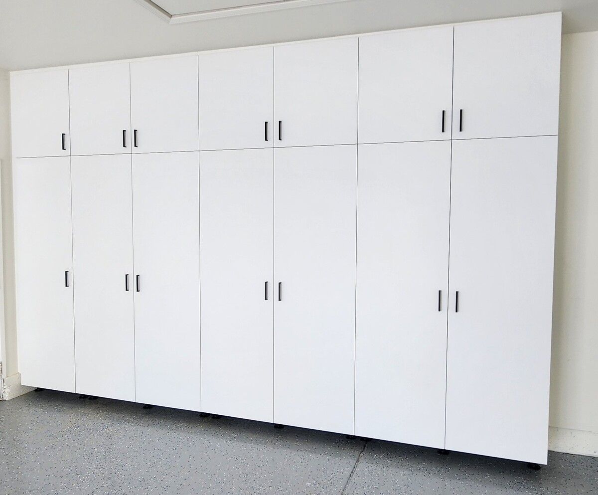 A wall of white cabinets in a garage with a gray floor.
