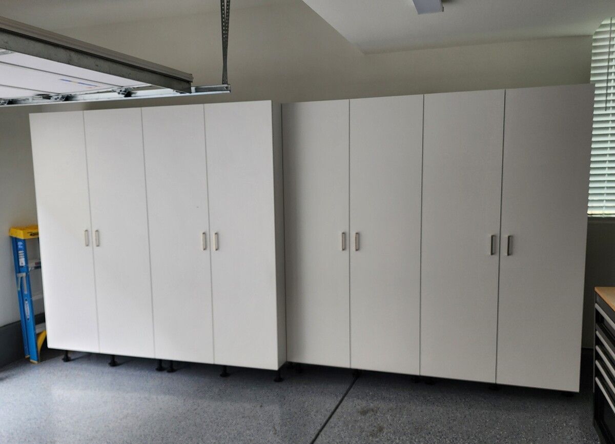 A garage with lots of white cabinets and a ladder