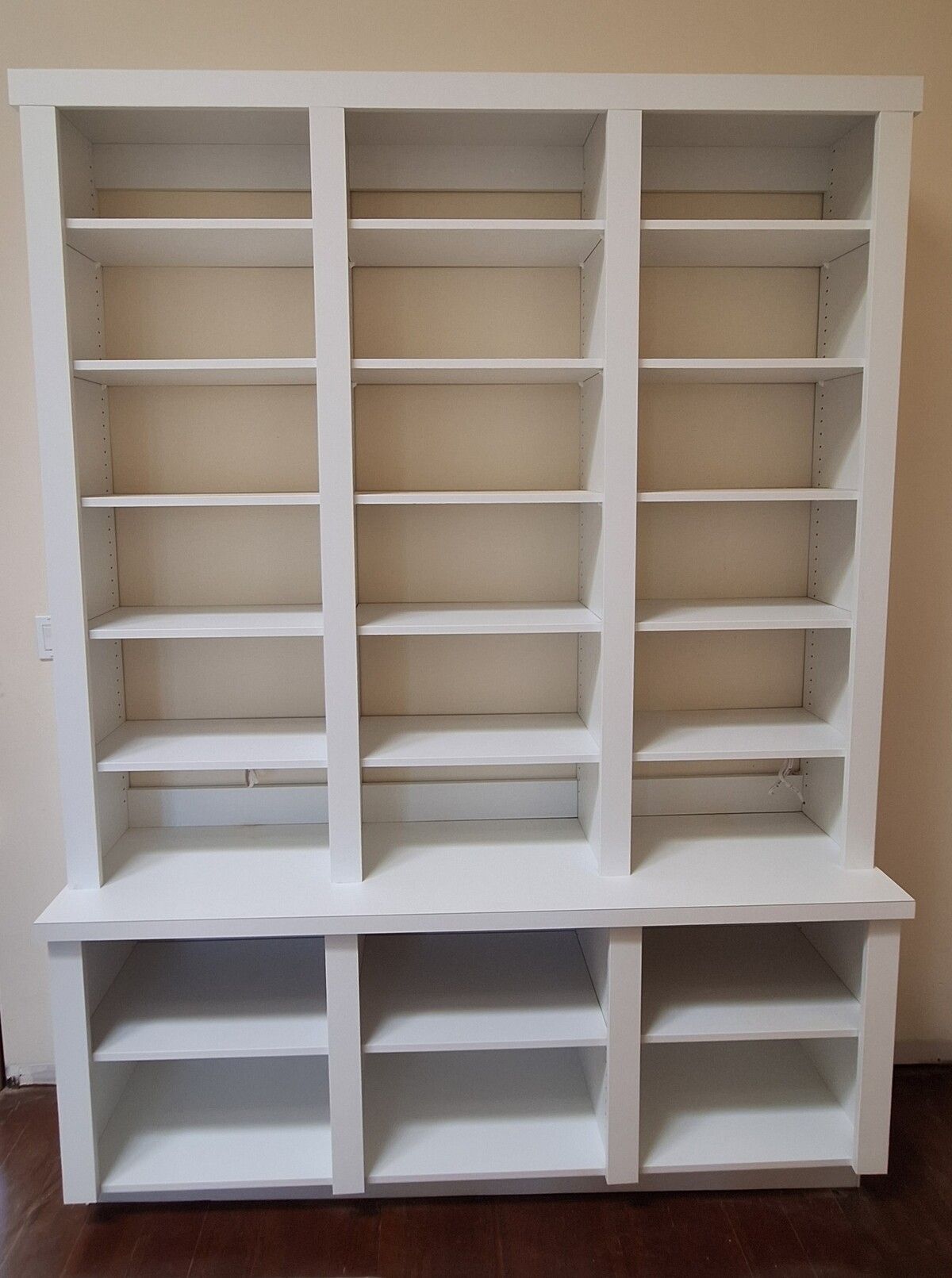 A white bookshelf with lots of shelves is sitting on a wooden floor in a room.