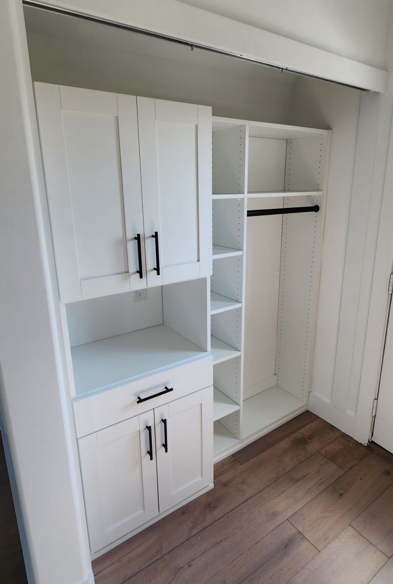 A closet with white cabinets and shelves and a wooden floor.