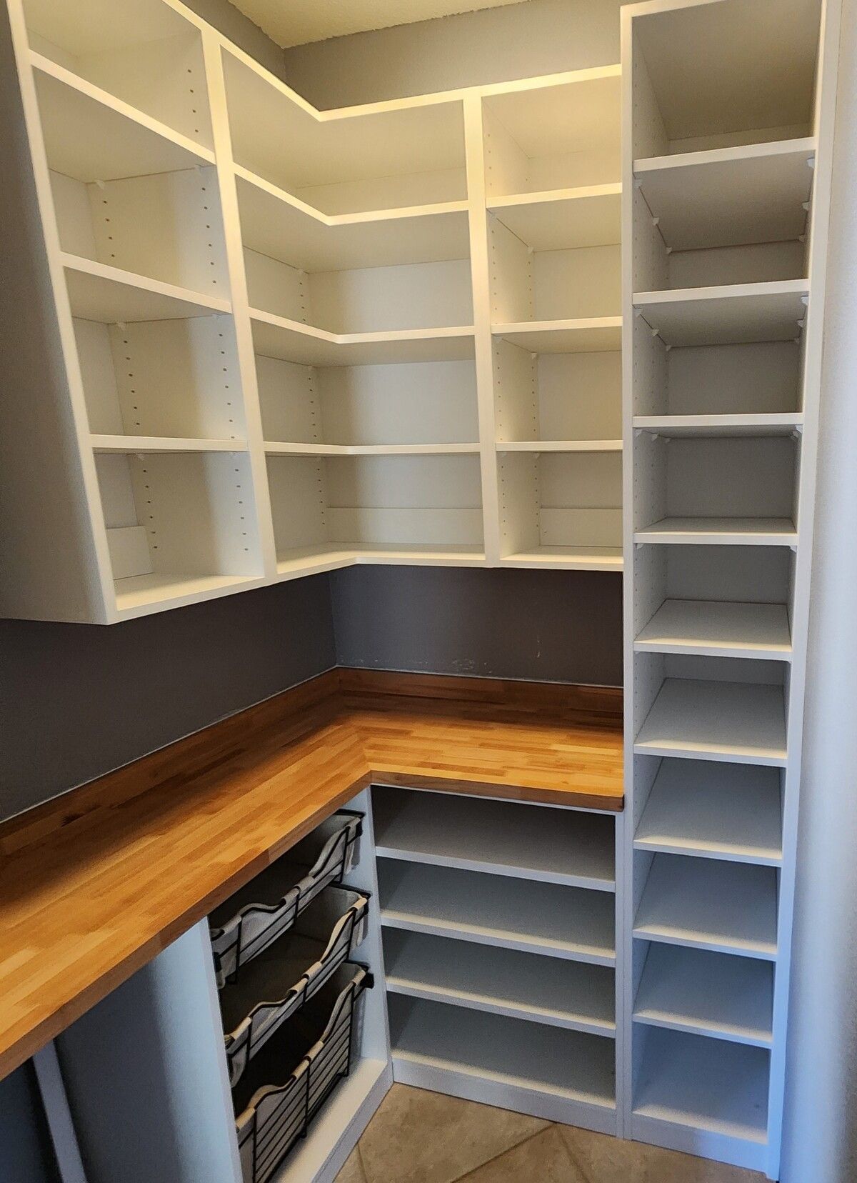 A pantry with white shelves and a wooden counter top.