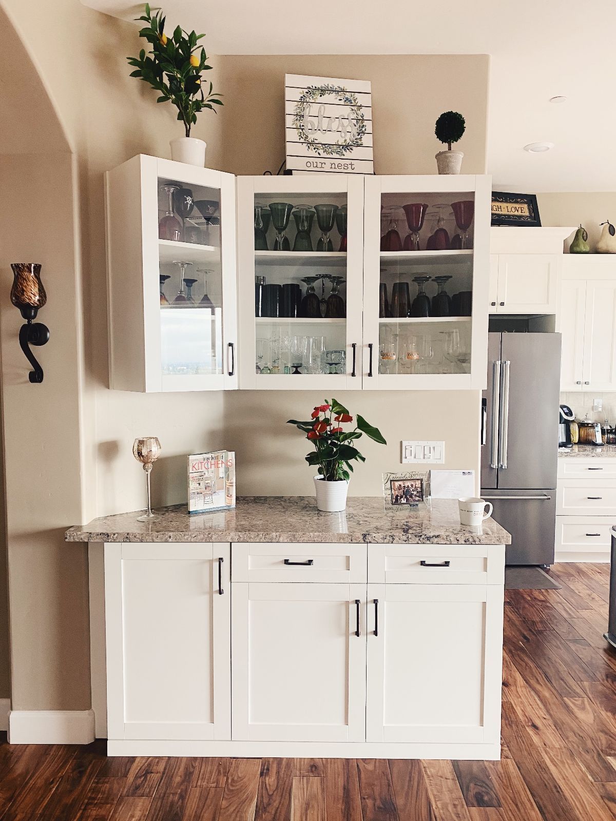 White kitchen cabinets with glass doors, granite countertop, and wooden floor.