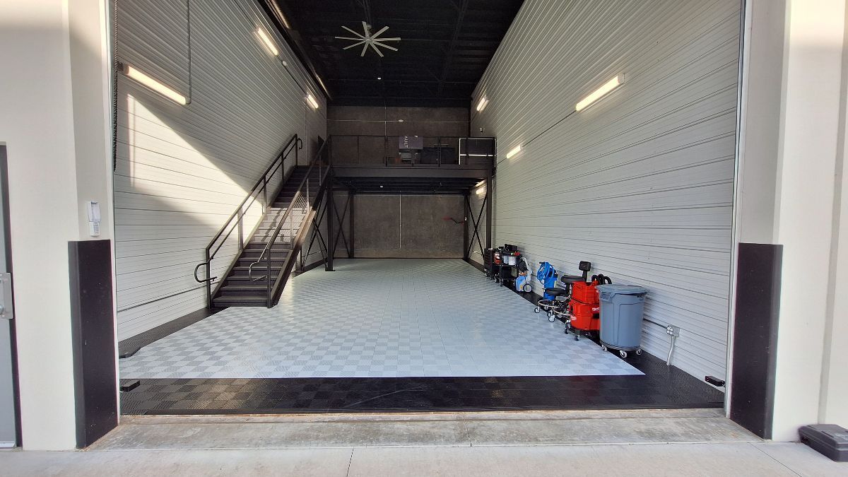 Open garage interior with a raised platform, stairs, and tools. White walls, black ceiling.