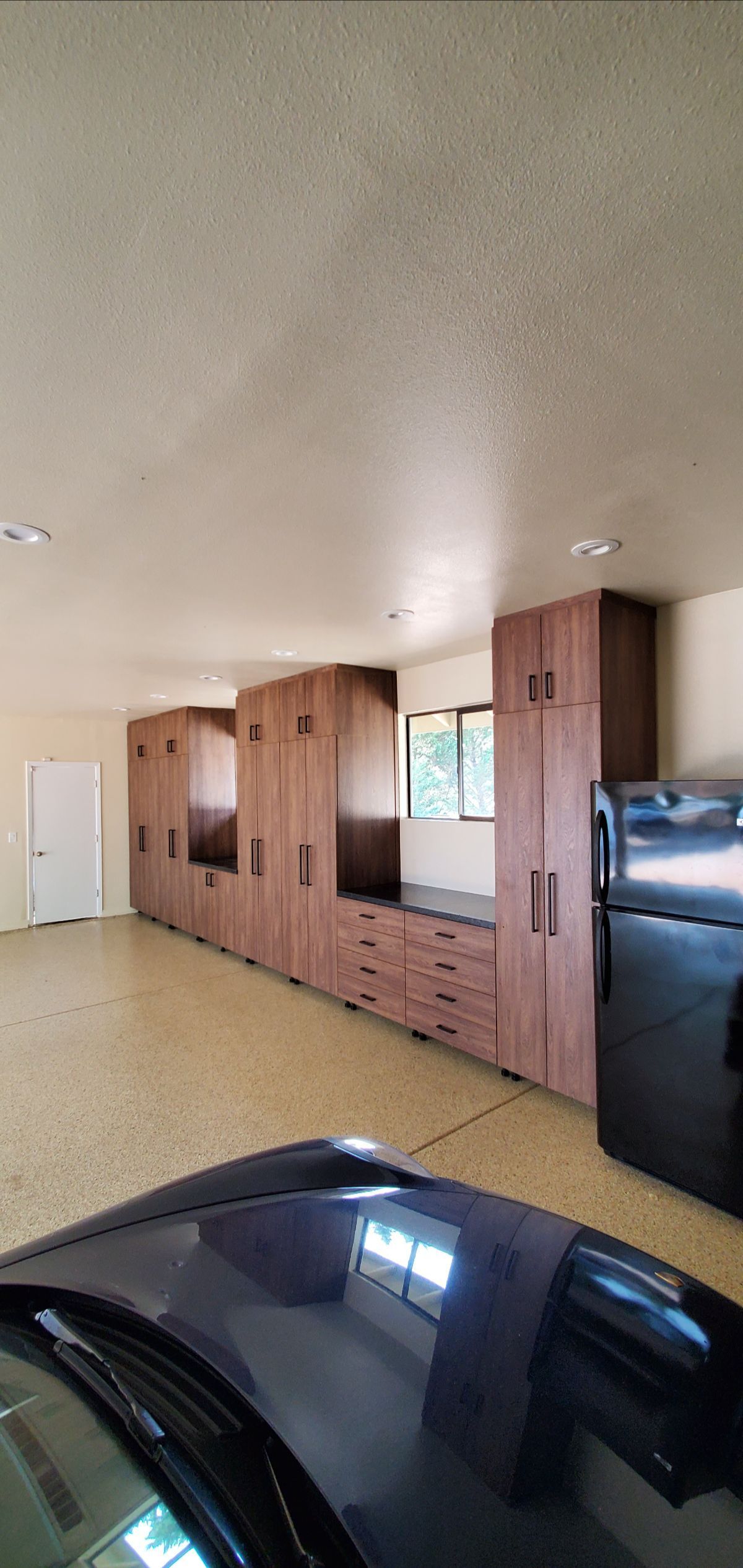 A garage with built-in wooden cabinets along the wall, a refrigerator, and a dark car.