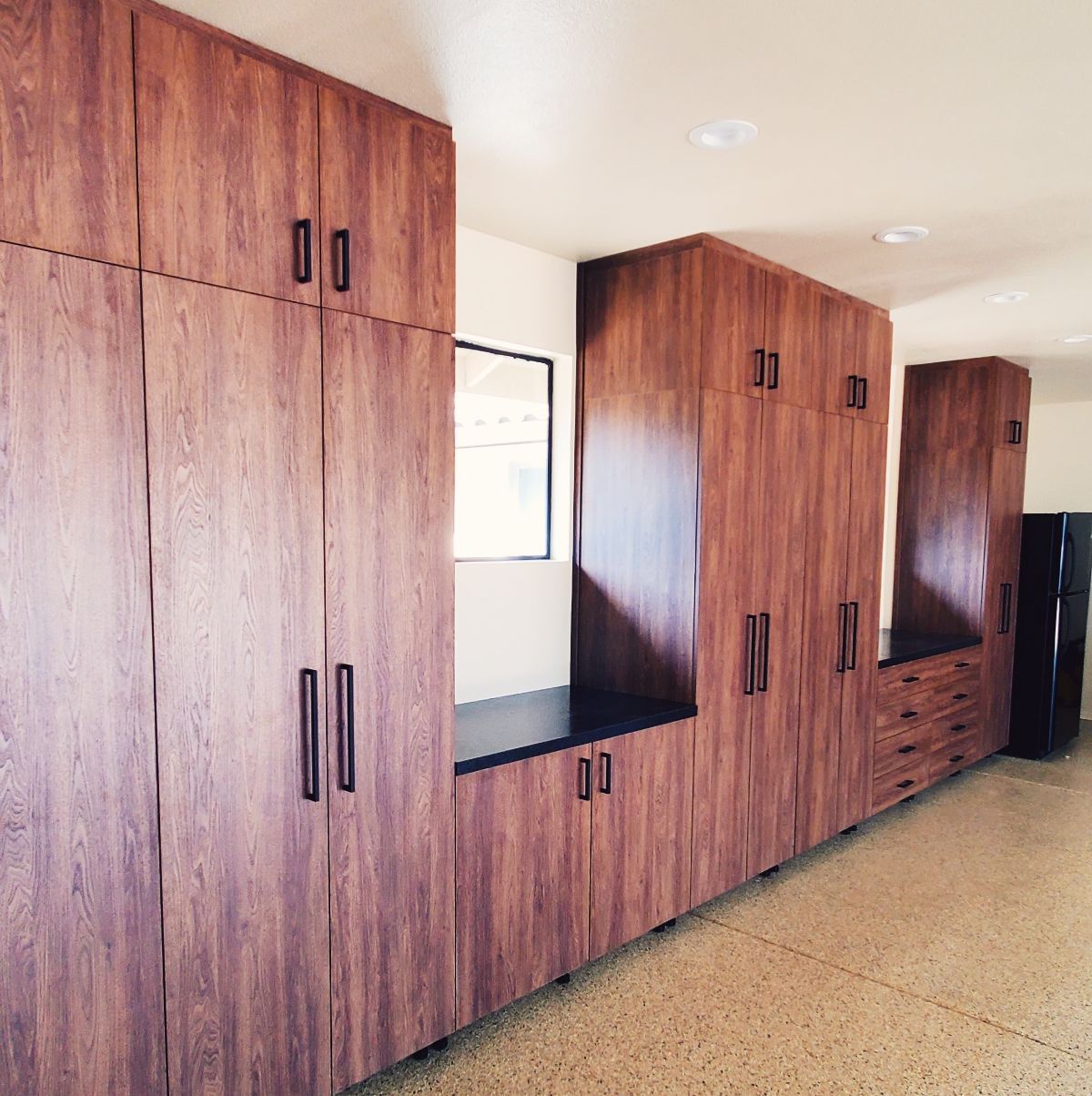Wooden storage cabinets in a room, with a dark countertop and black hardware.