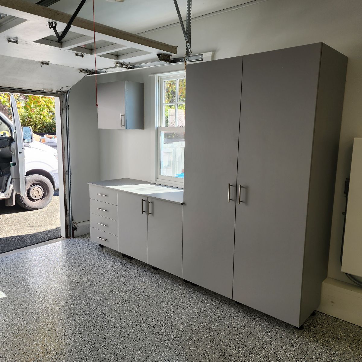 Garage with gray cabinets and epoxy floor. A van is parked outside the open garage door.