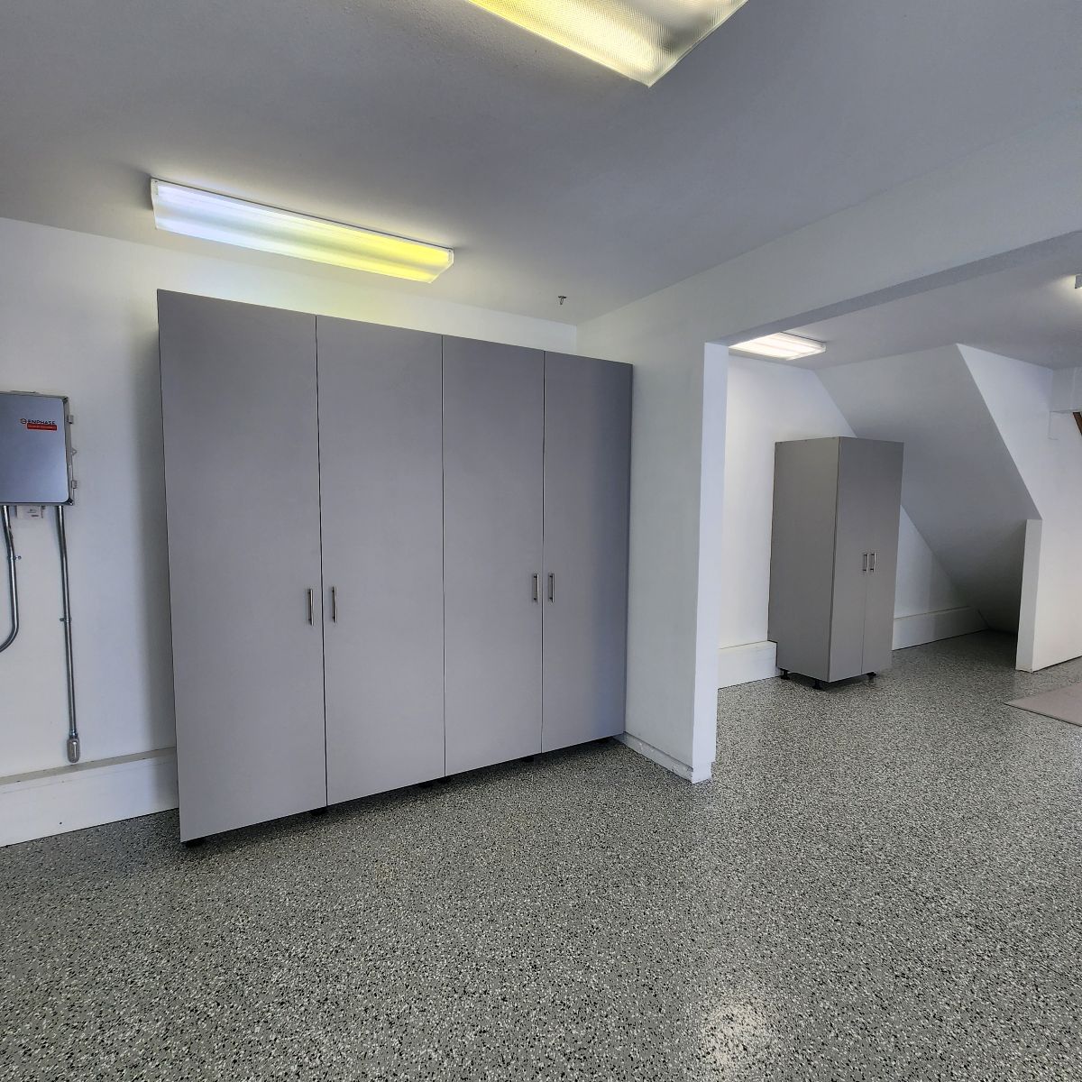 Garage interior with gray storage cabinets against a white wall and speckled floor.