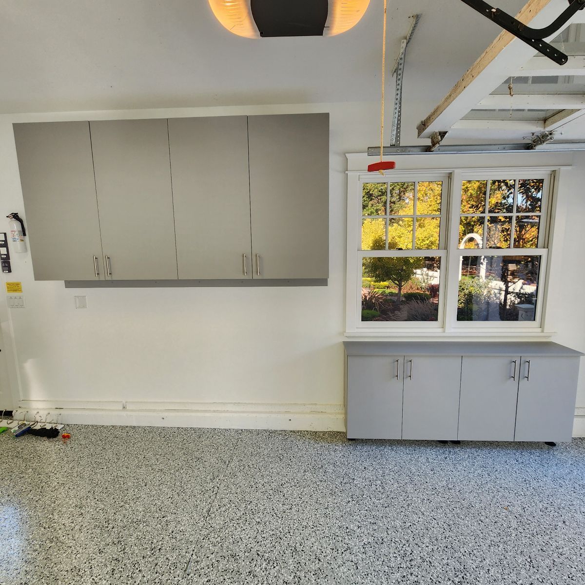 Garage with gray cabinets above and below a window, with a speckled floor.
