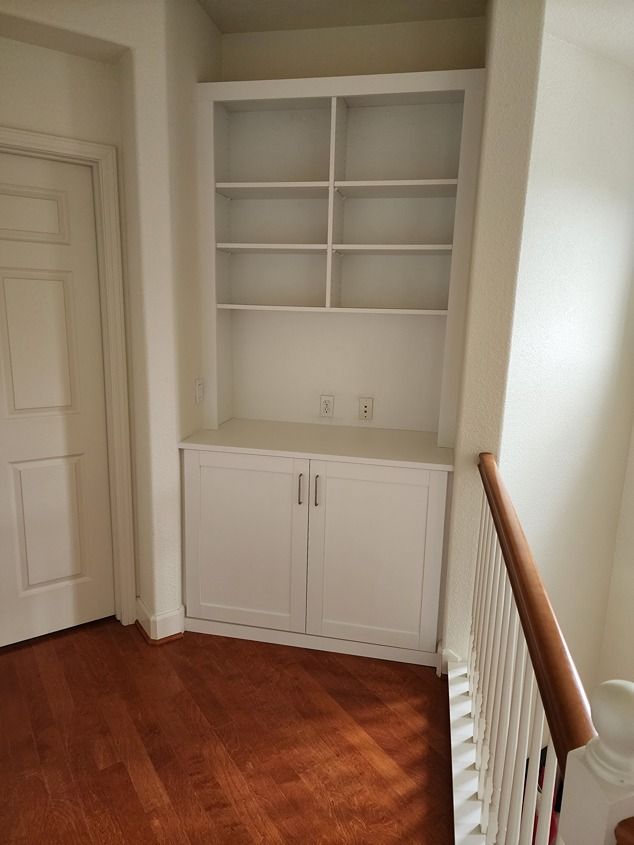 A hallway with a staircase and a bookshelf in the corner.