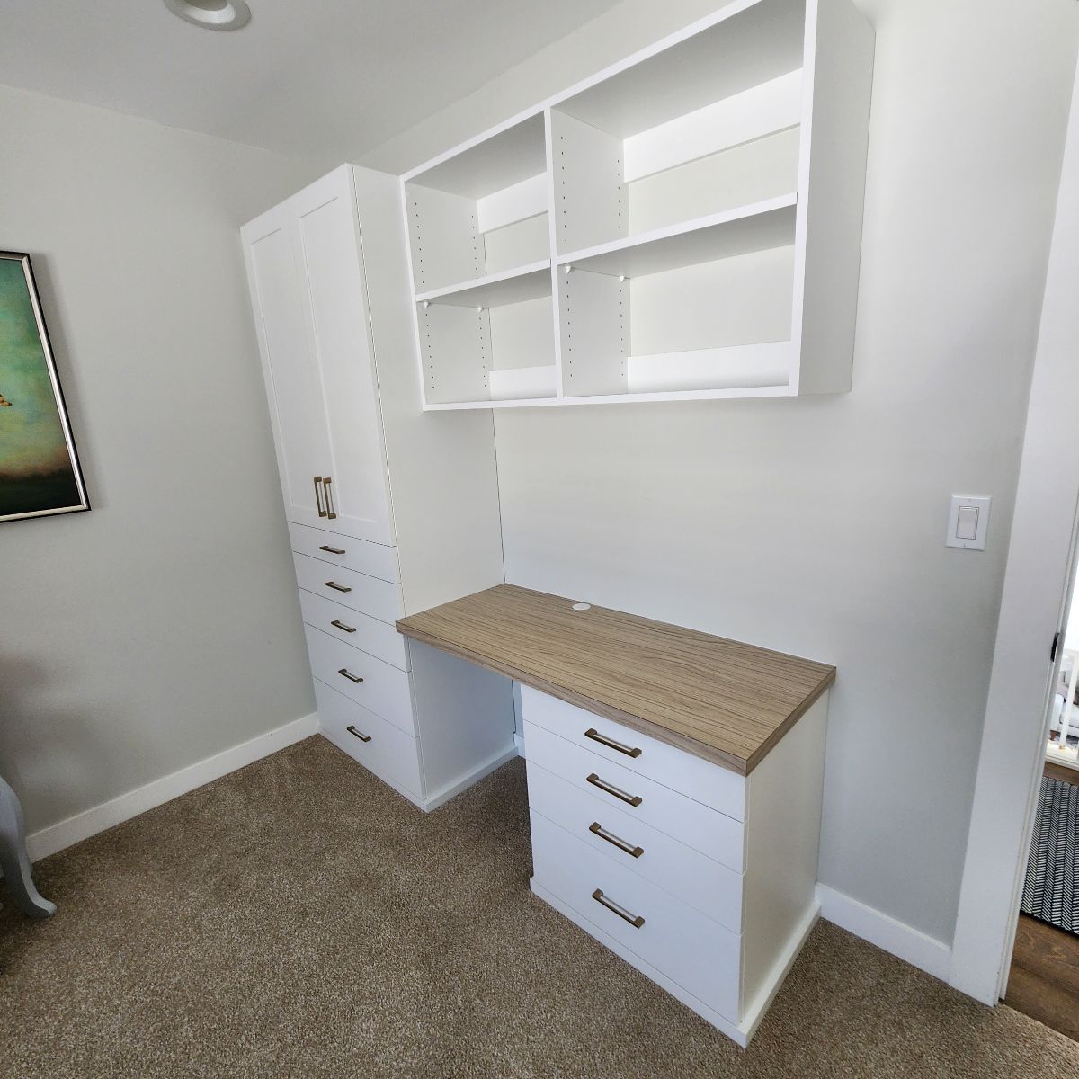 White desk with drawers and shelves mounted to a wall. A tall storage cabinet is to the left.