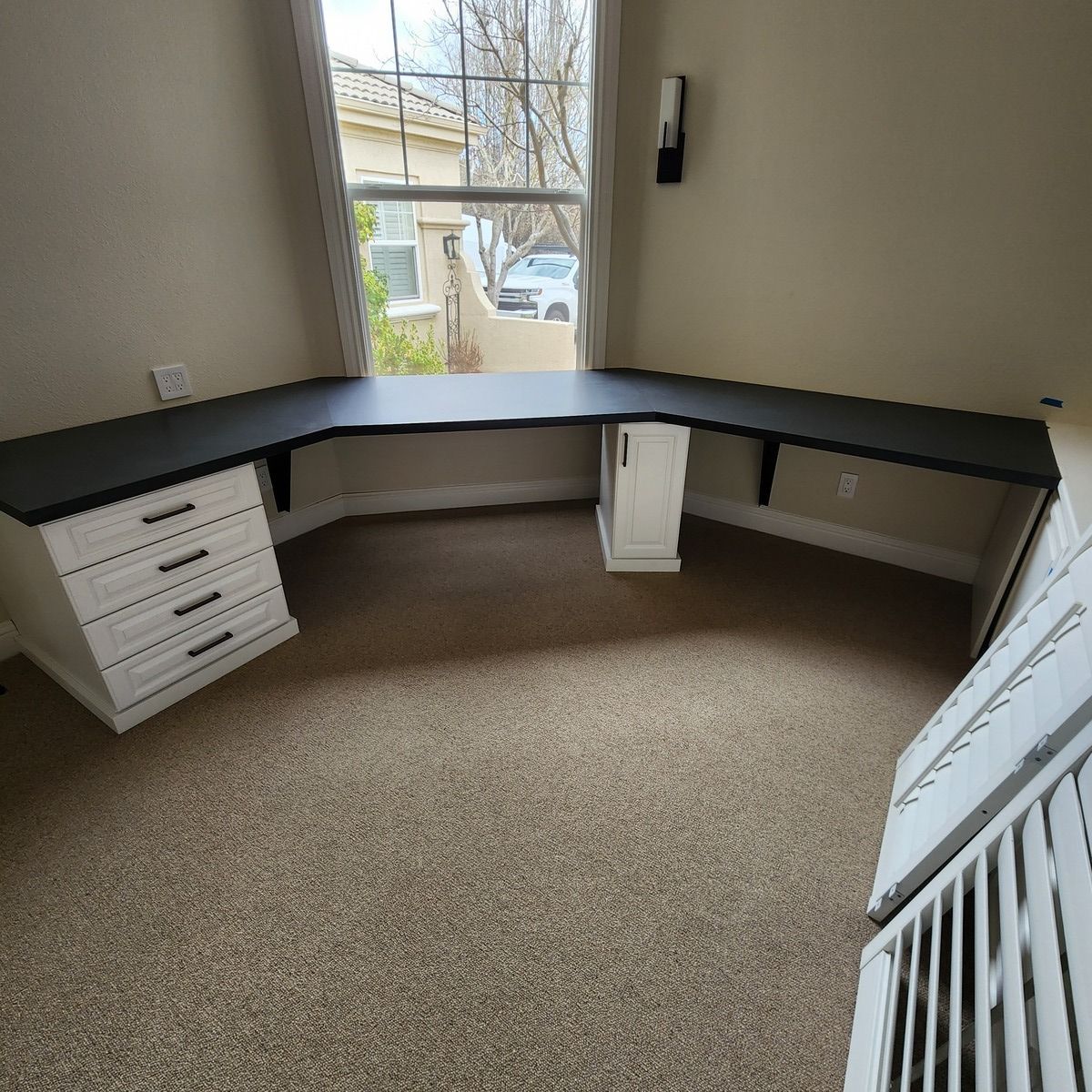 A  home office room with a desk and drawers in front of a window.