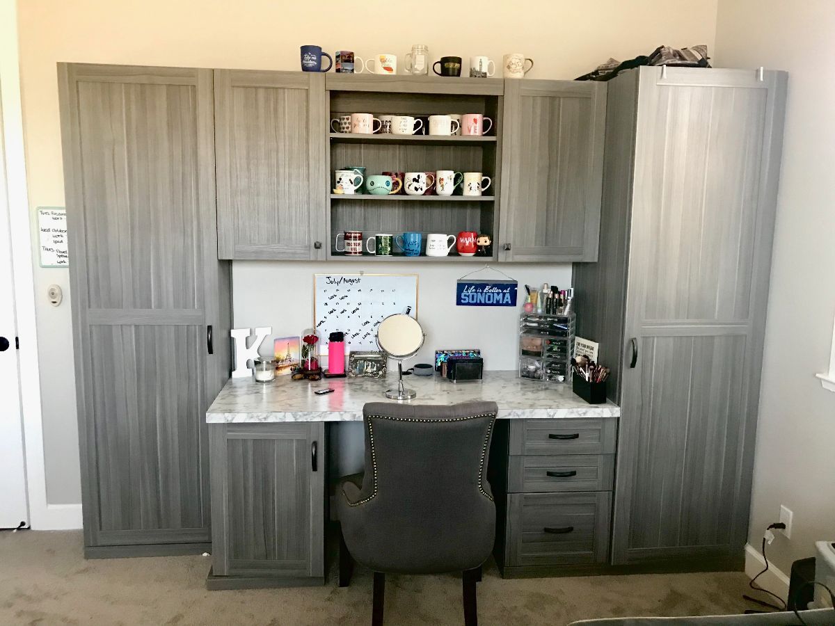 Gray home office desk with cabinets, shelves of mugs, and chair.