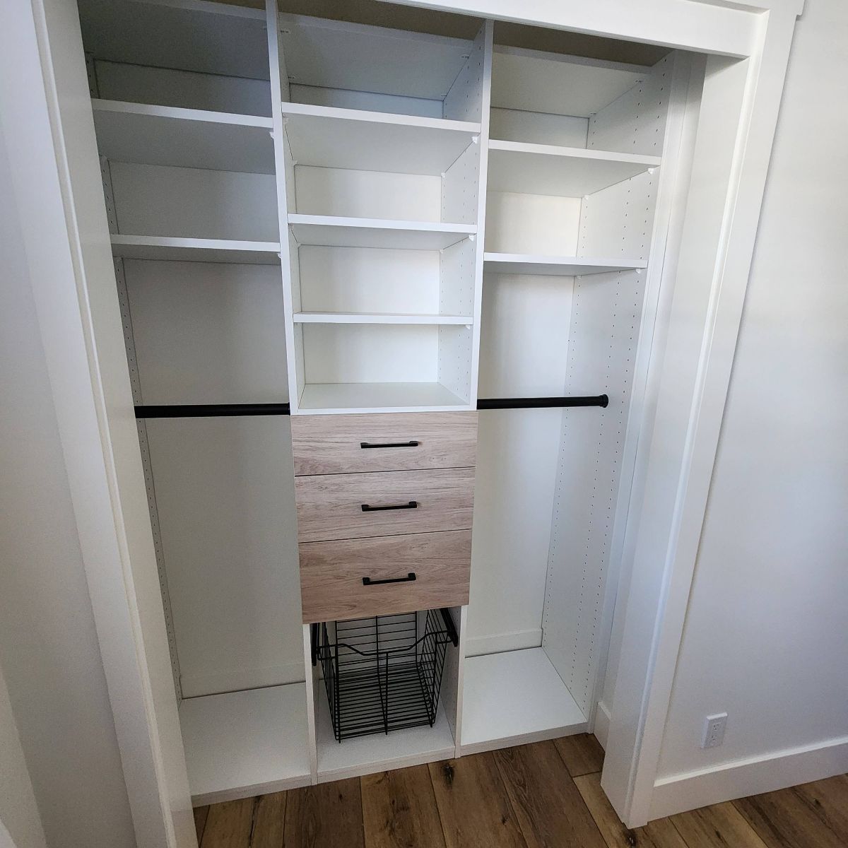 Reach in Closet interior with white shelves, drawers, and black rods for hanging clothes; a wire basket on the floor.
