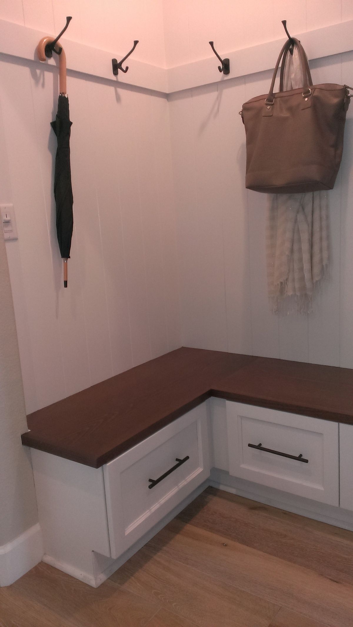 A hallway with a bench , hooks , and a bag hanging on the wall.