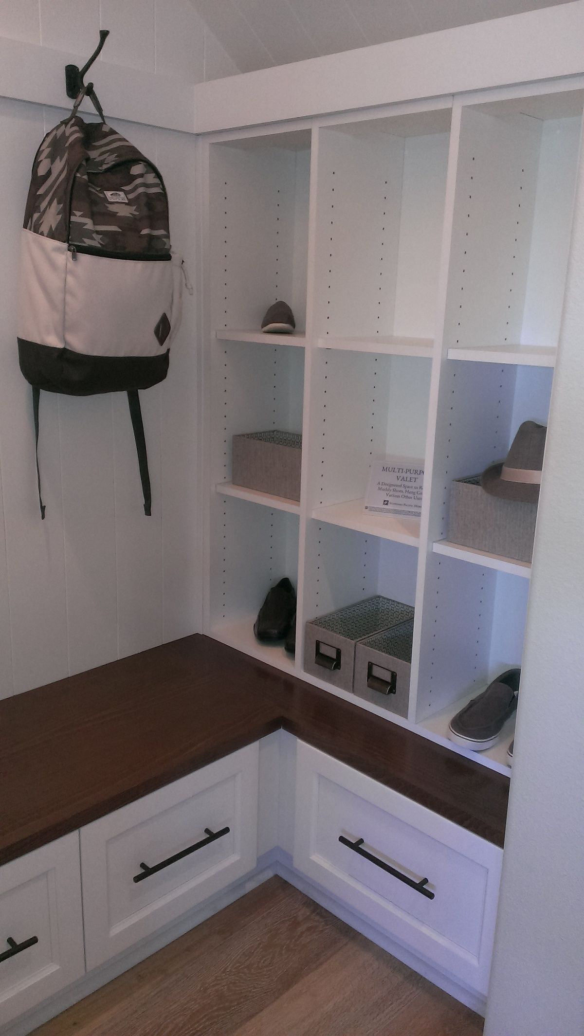 A room with a bench and shelves and a backpack hanging on the wall.
