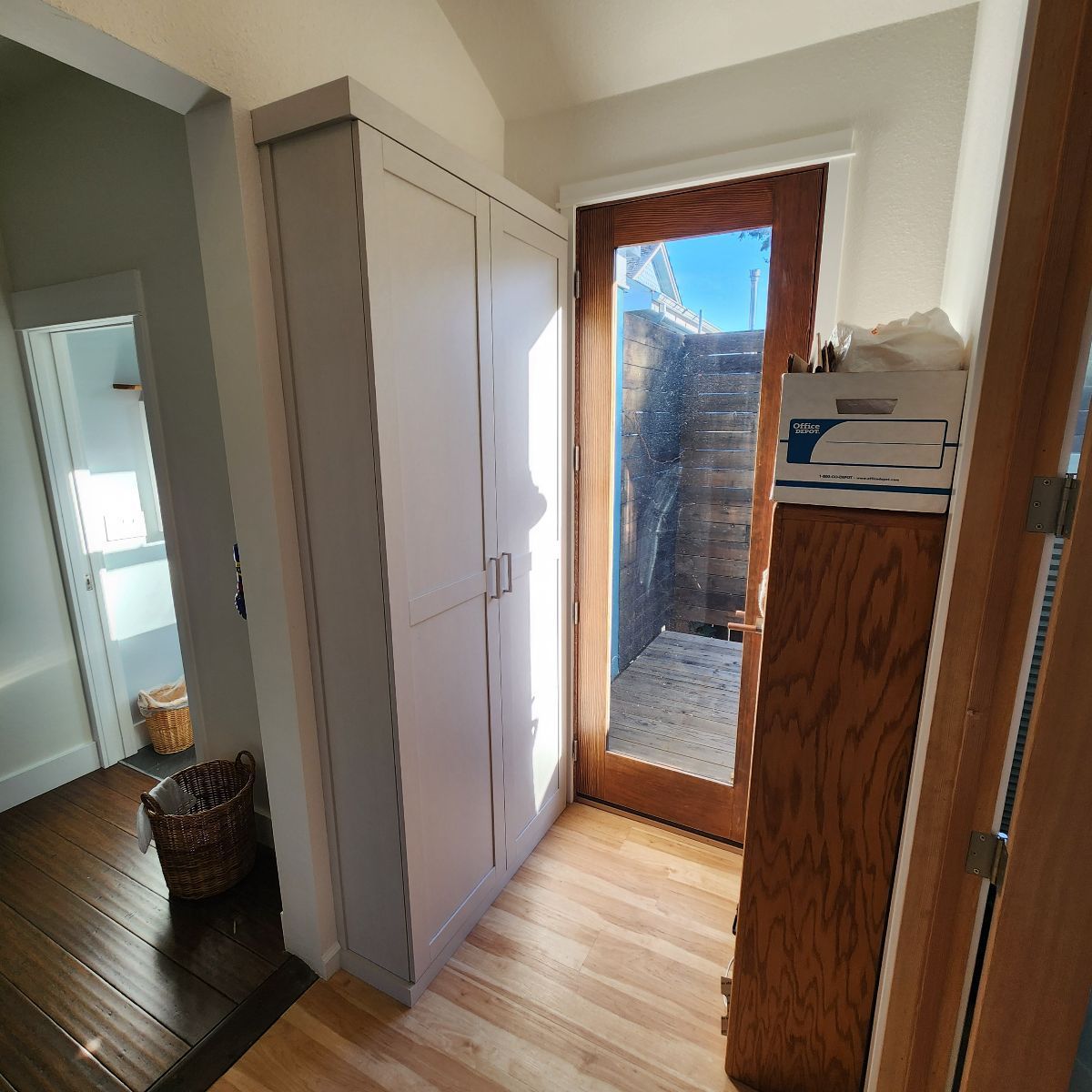 Hallway with a gray cabinet, wooden door and window, and a glimpse into another room with a basket.