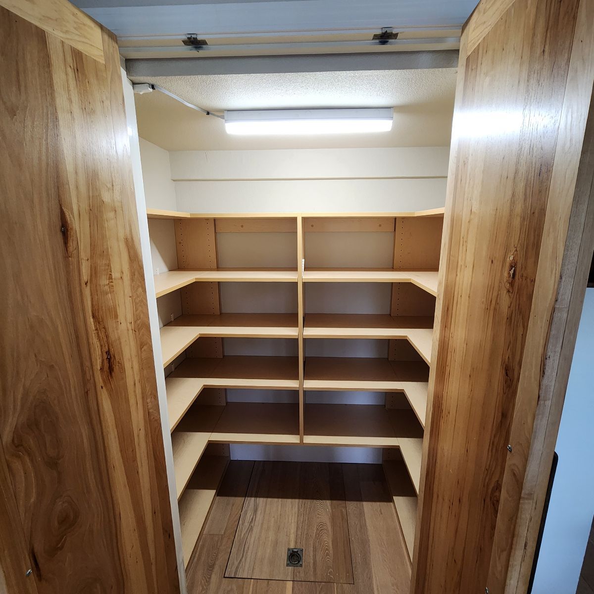 Wooden pantry with open shelves, wooden doors, and a fluorescent light.
