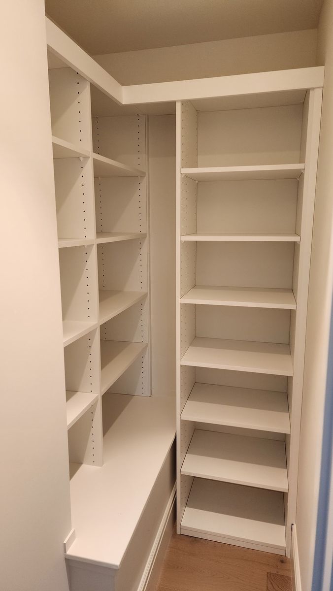A walk in closet with lots of shelves and a bench.