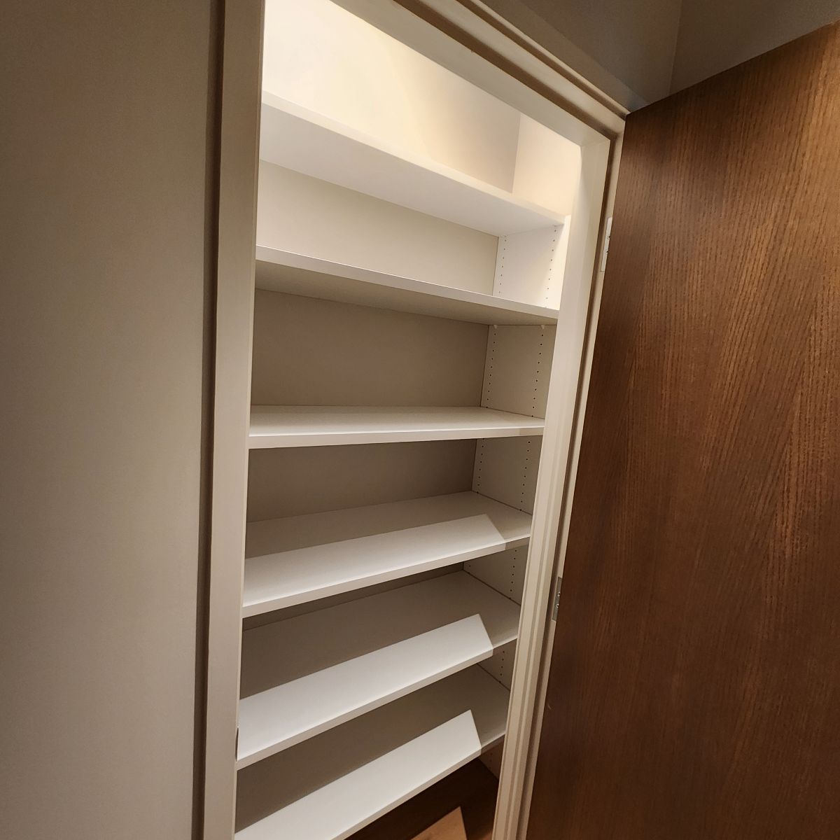 Empty white shelves inside a closet with a wooden door.