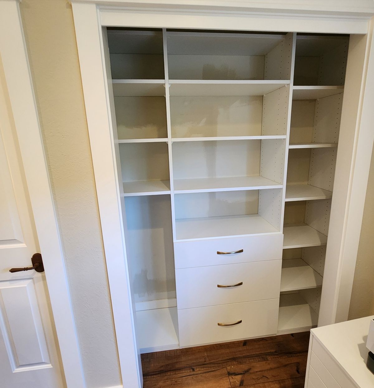 White built-in closet with shelves and drawers.  Wooden floor, neutral walls.