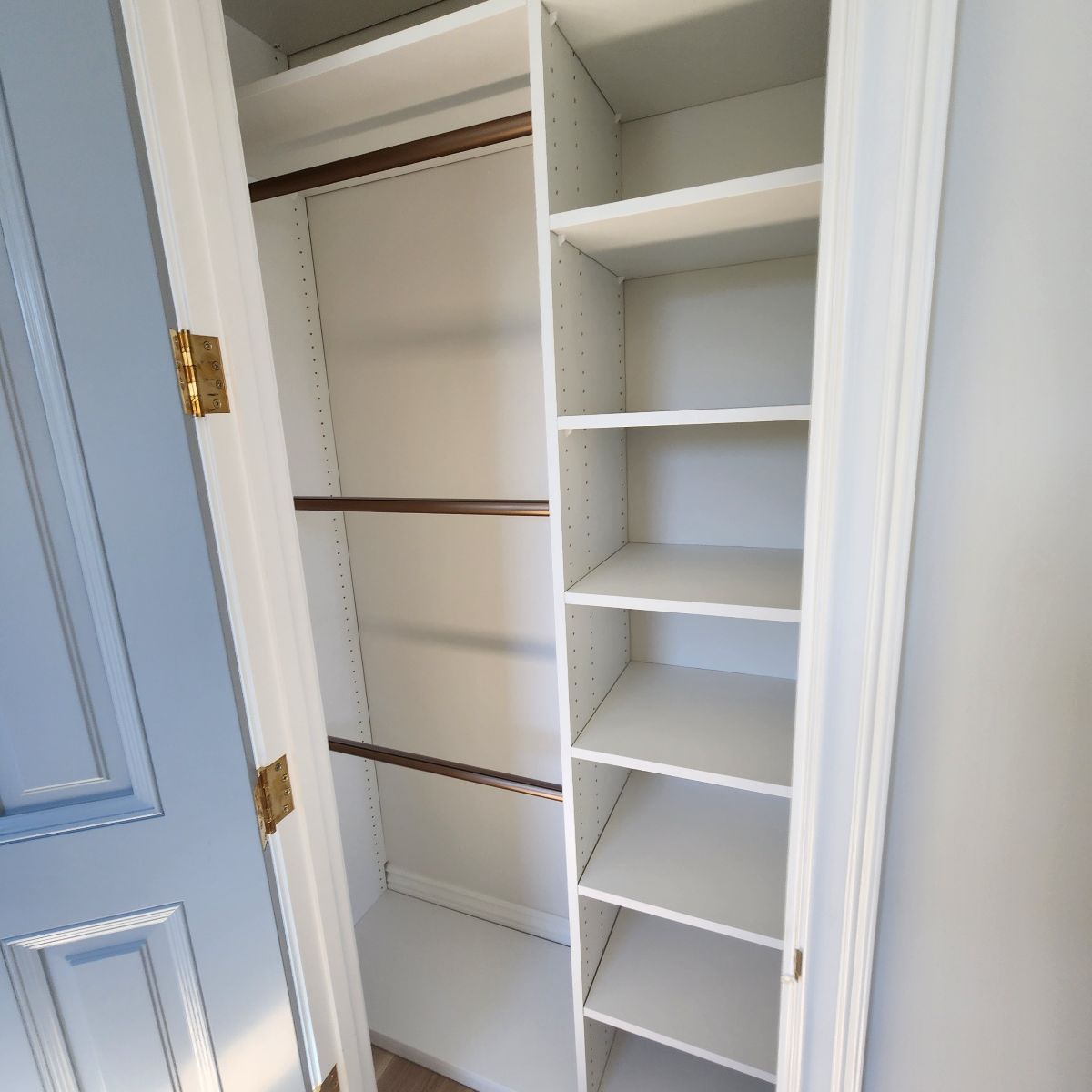 White Reach In  closet interior with shelves and rods, door ajar, blue door frame, neutral wall.