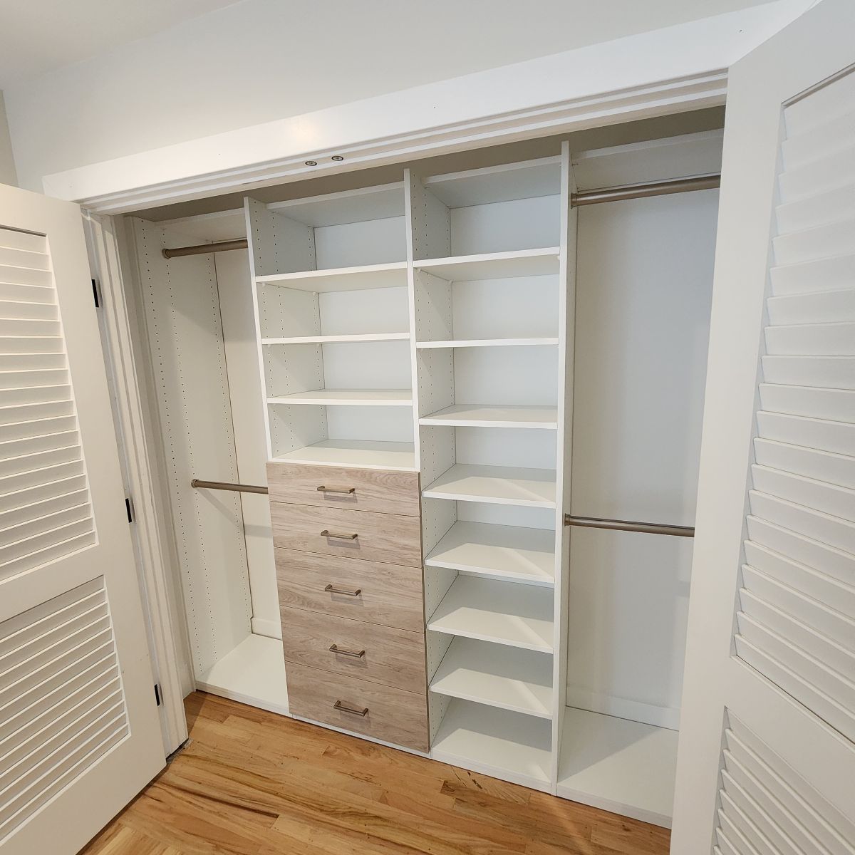 Open white closet with shelves, drawers, and hanging rods. Interior has wooden floors.