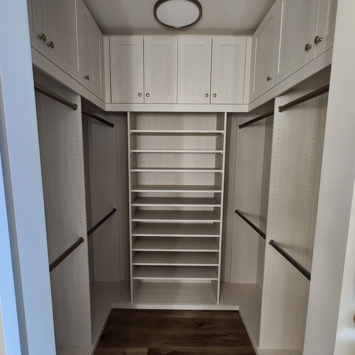 Walk-in closet with white cabinets, shelves, and rods, centered shoe rack, and wood-look floor.