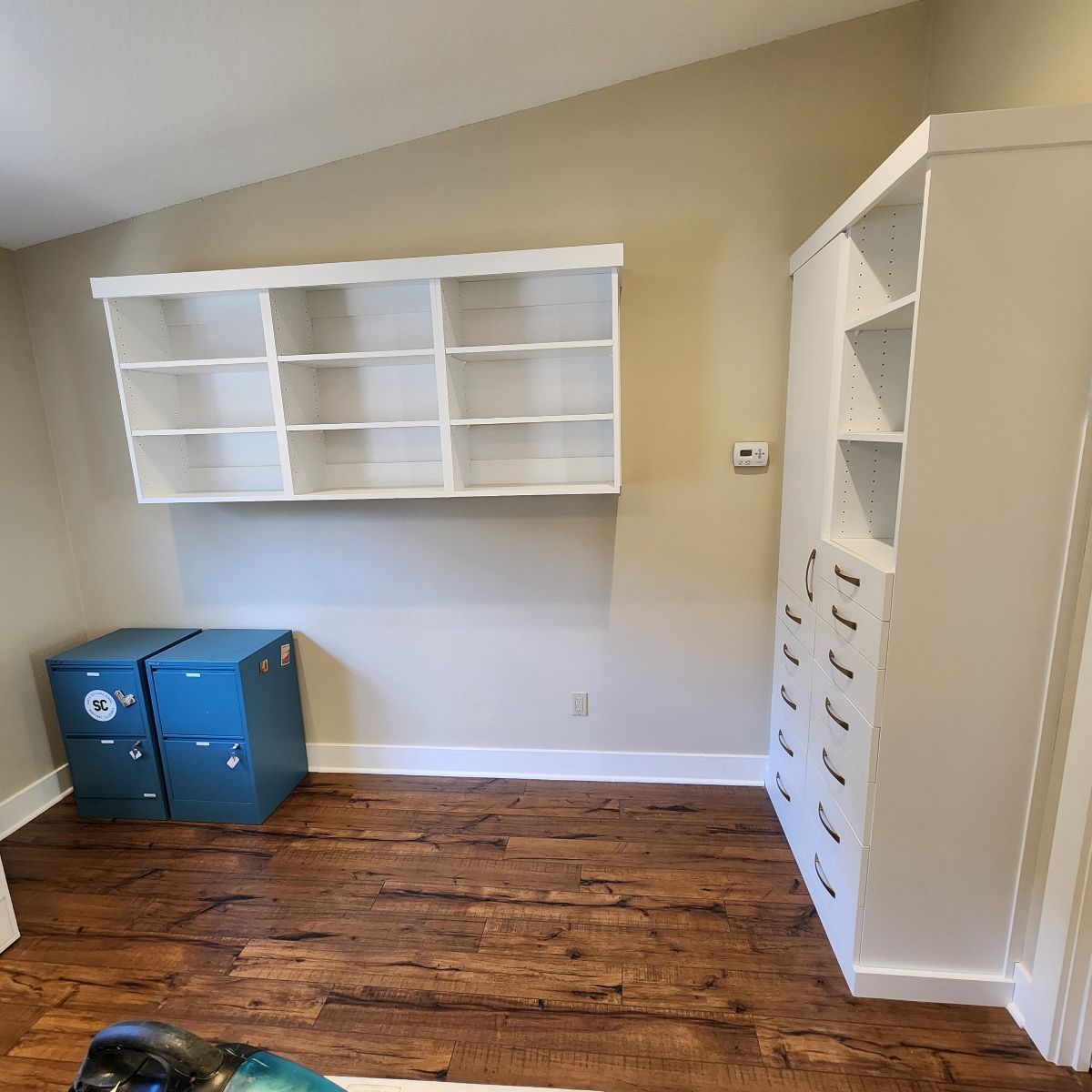 A room with white shelving and cabinets, blue file cabinets, and wood flooring.