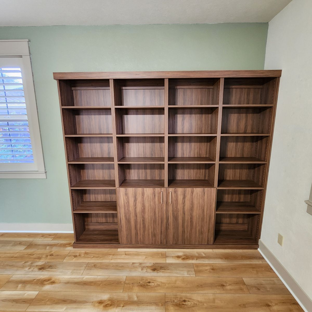 Brown wooden bookcase with multiple shelves and cabinets against a green wall.
