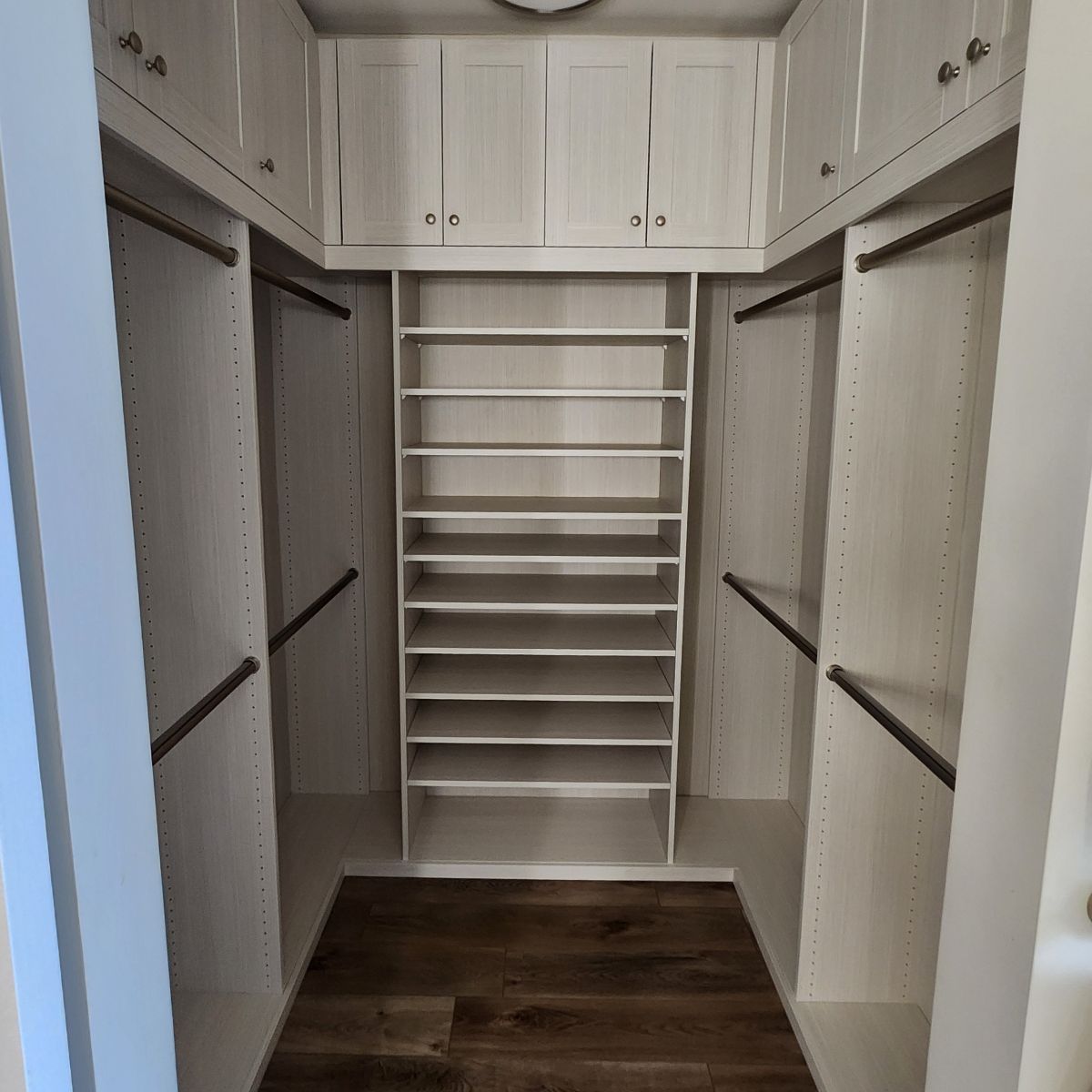 Walk-in closet with white shelves and cabinets, shoe rack, and dark wood floor.