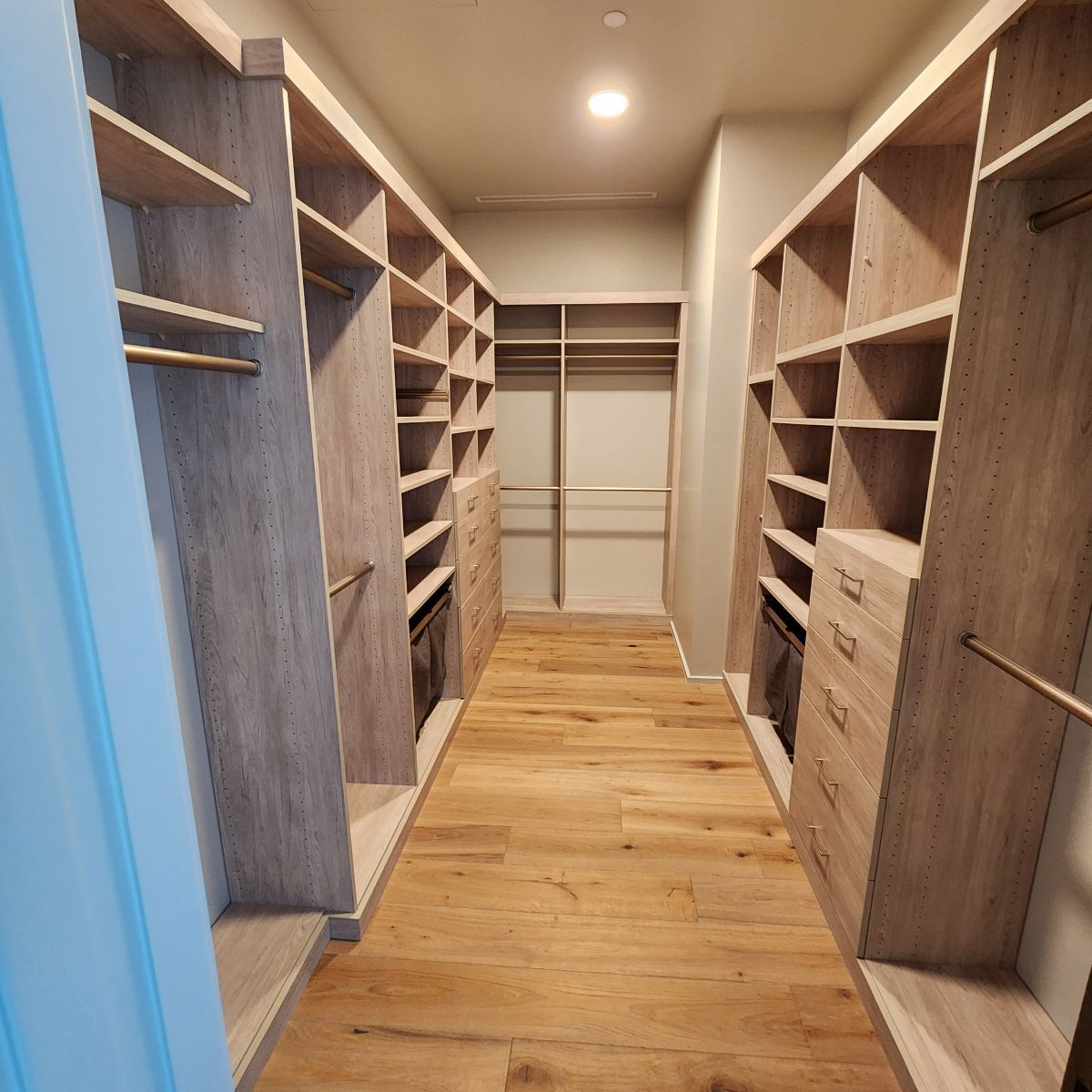 Walk-in closet with light wood shelving and drawers, long narrow space with hardwood floors.