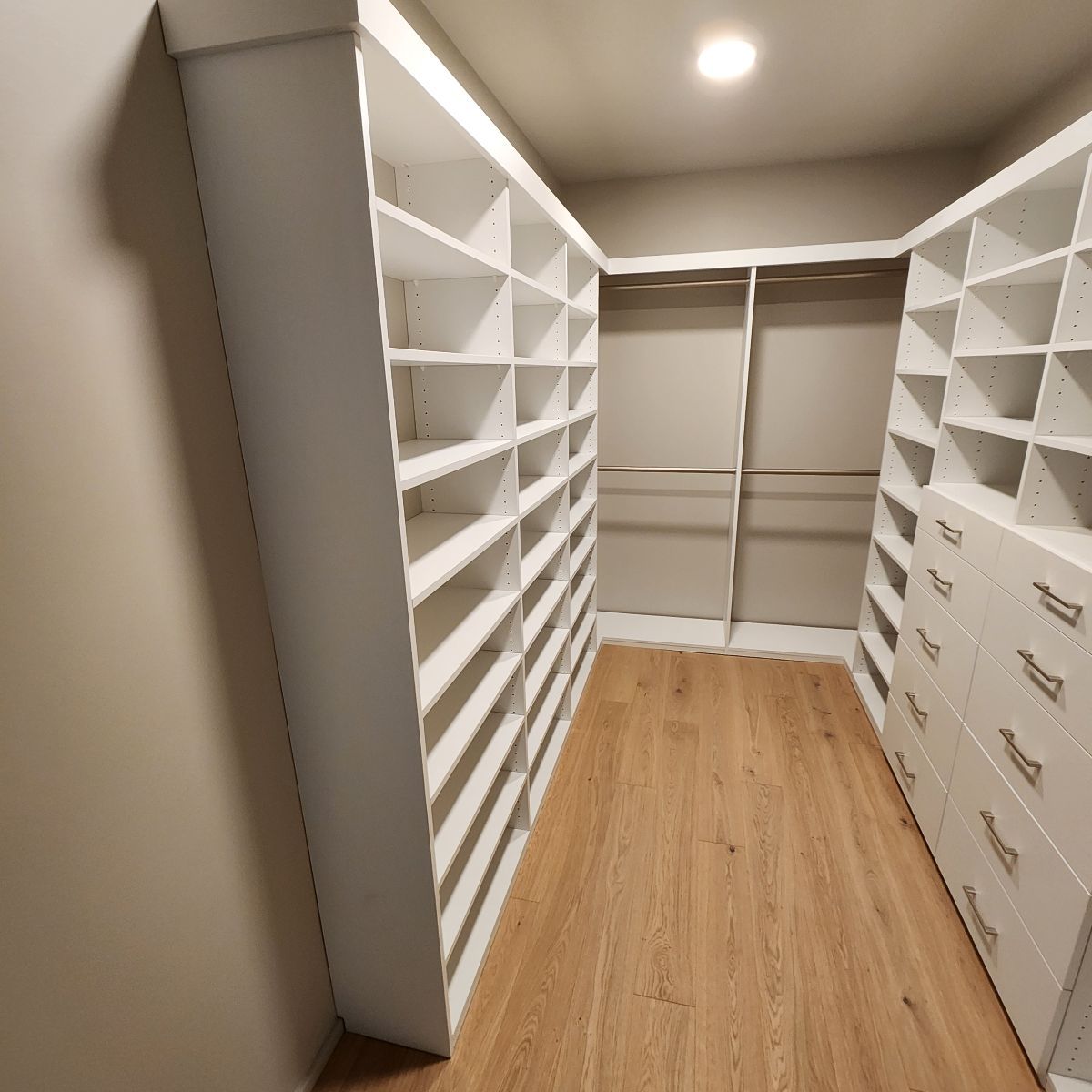 Walk-in closet with white shelving, drawers, and wood floors.