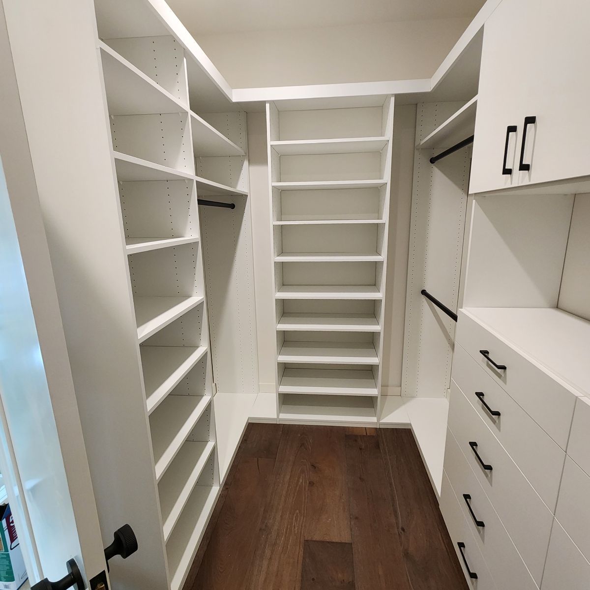 Walk-in closet with white shelving, cabinets, and dark wood floors.