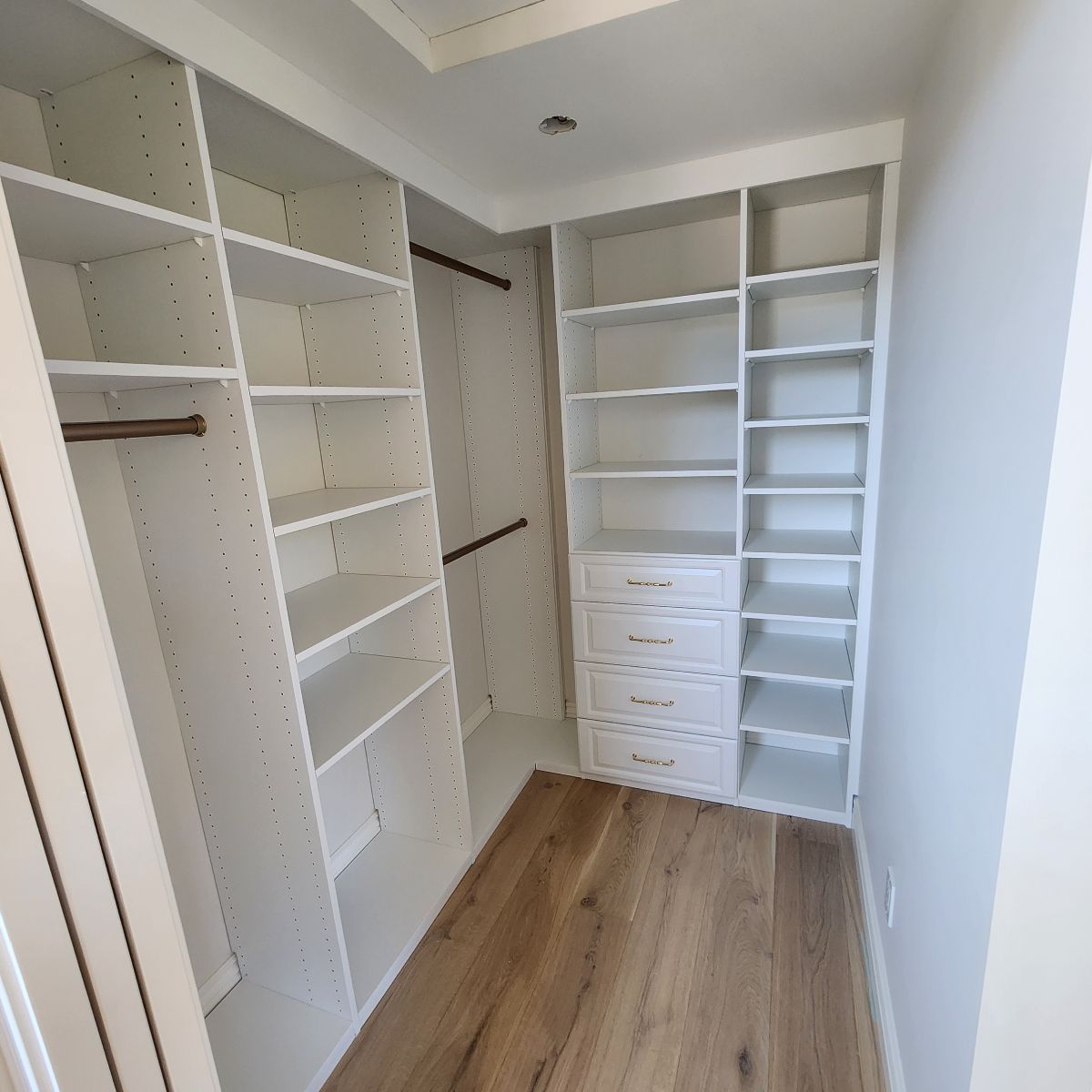 A walk-in closet with white shelving units and wooden floors.