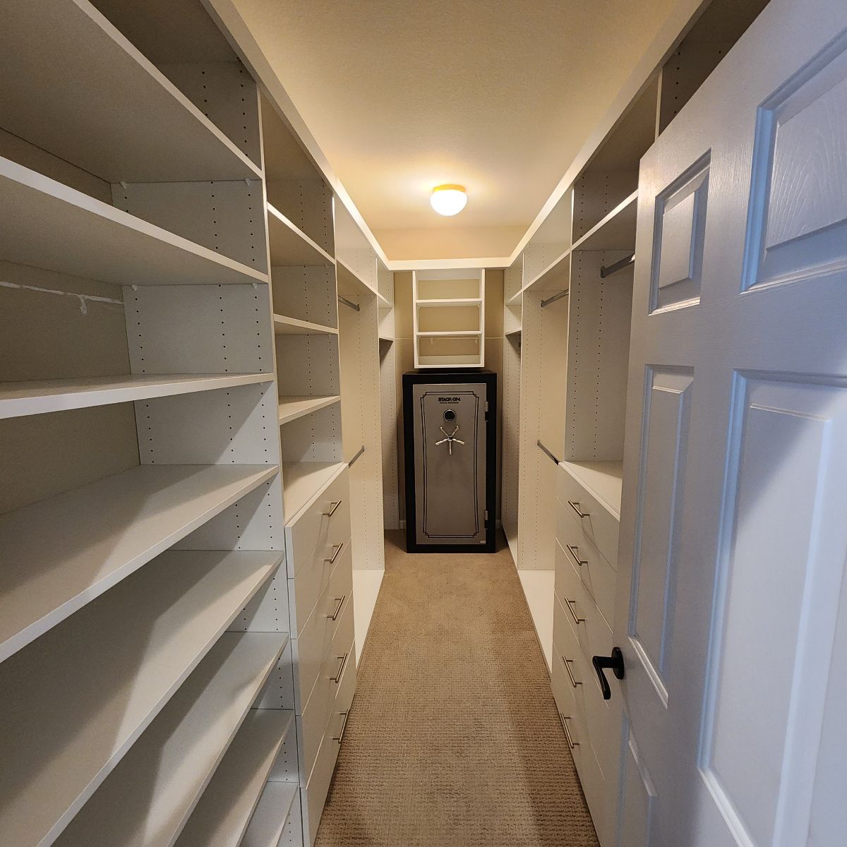 Walk-in closet with shelves on both sides, safe at the back, and a door on the right.