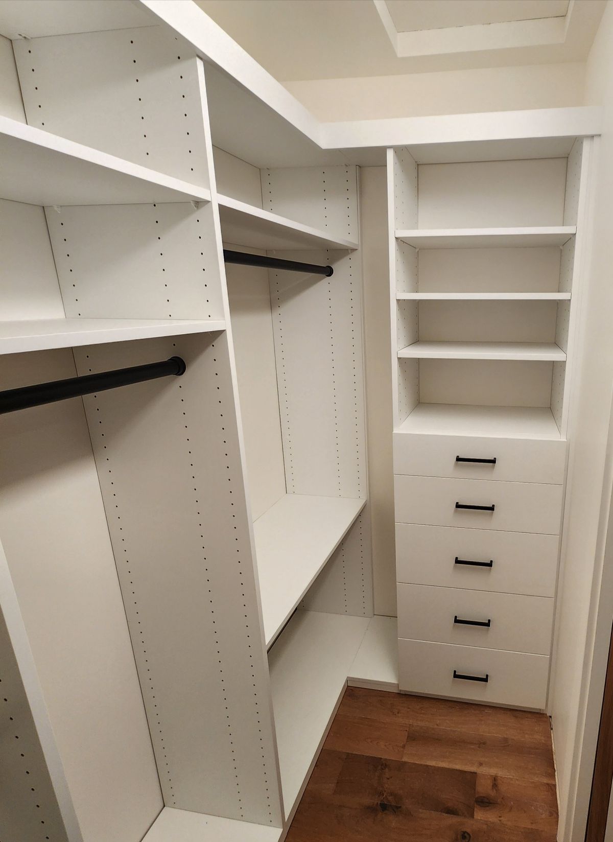White walk-in closet with shelves, drawers, and hanging rods. Hardwood floor.