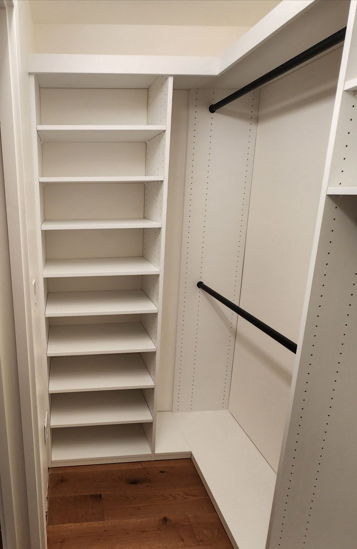 White built-in closet with shelves and hanging rods; wooden floor.