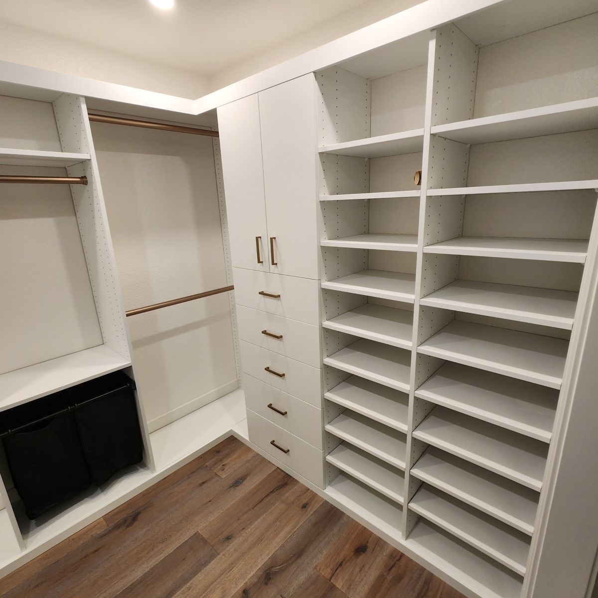 White closet with shelves, drawers, and hanging rods. Light brown wood floor.