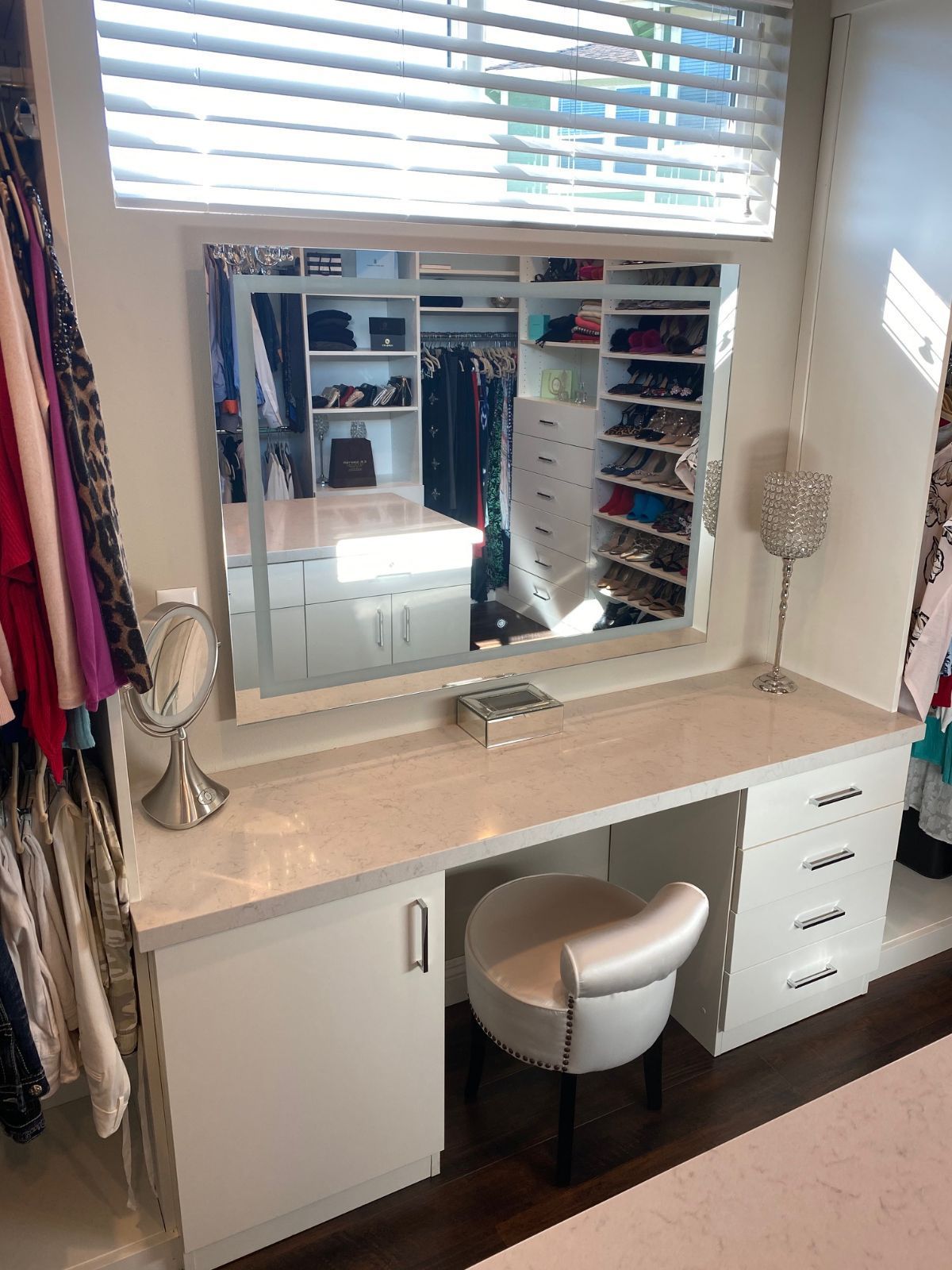 Vanity desk in a white closet with a large mirror and an upholstered chair.