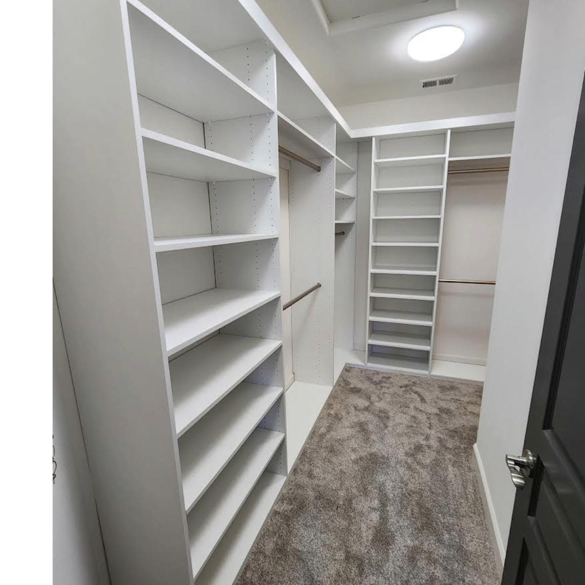 Walk-in closet with white shelving, tan rug, and open doorway with dark door.