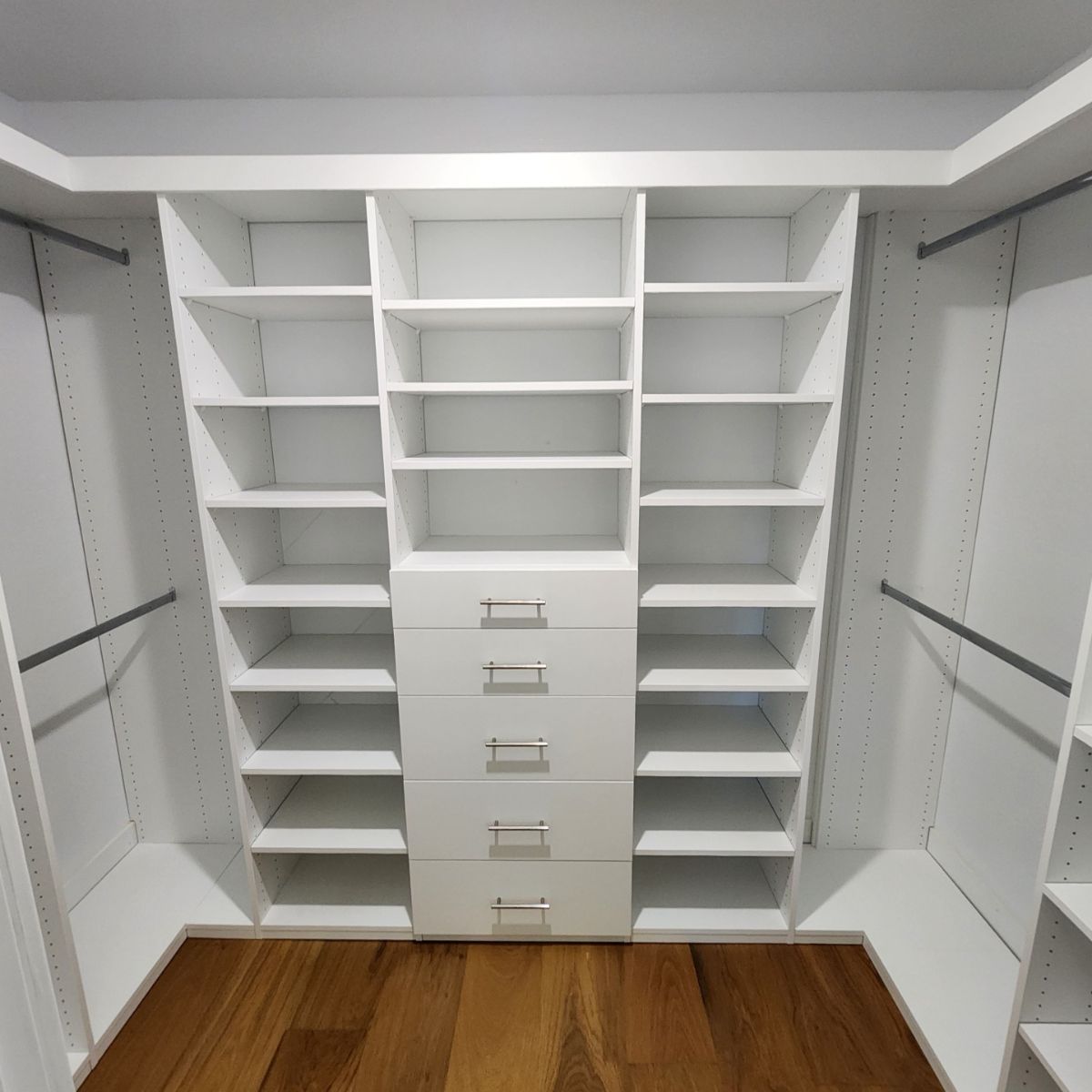 White custom walk-in closet with shelving, drawers, and clothing rods, wooden floor, empty.