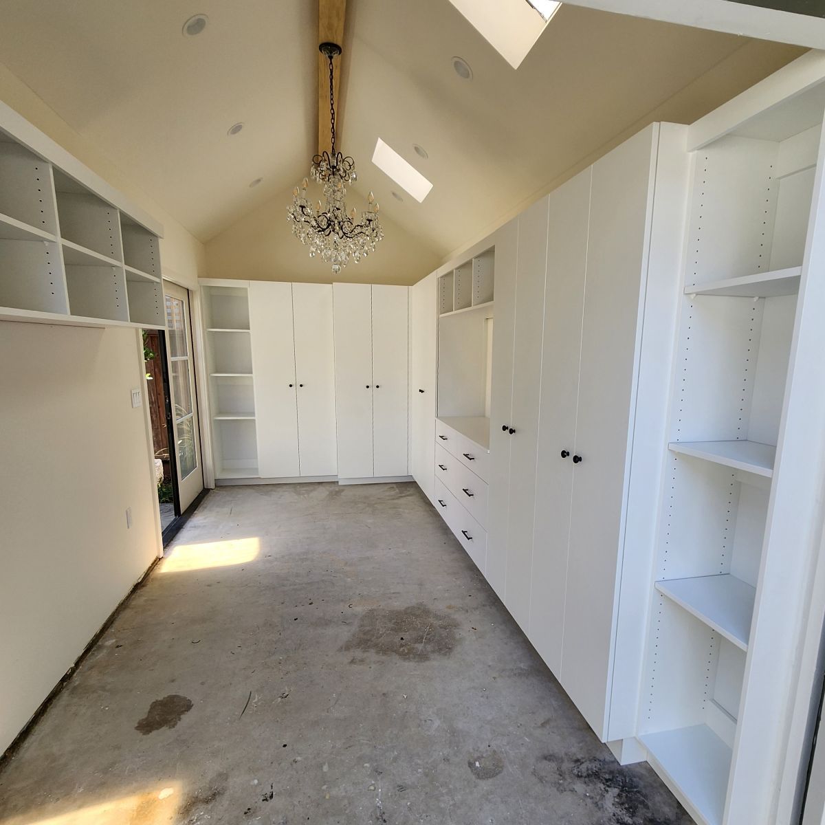 White closet interior with built-in cabinets, shelving, a chandelier, and a concrete floor.